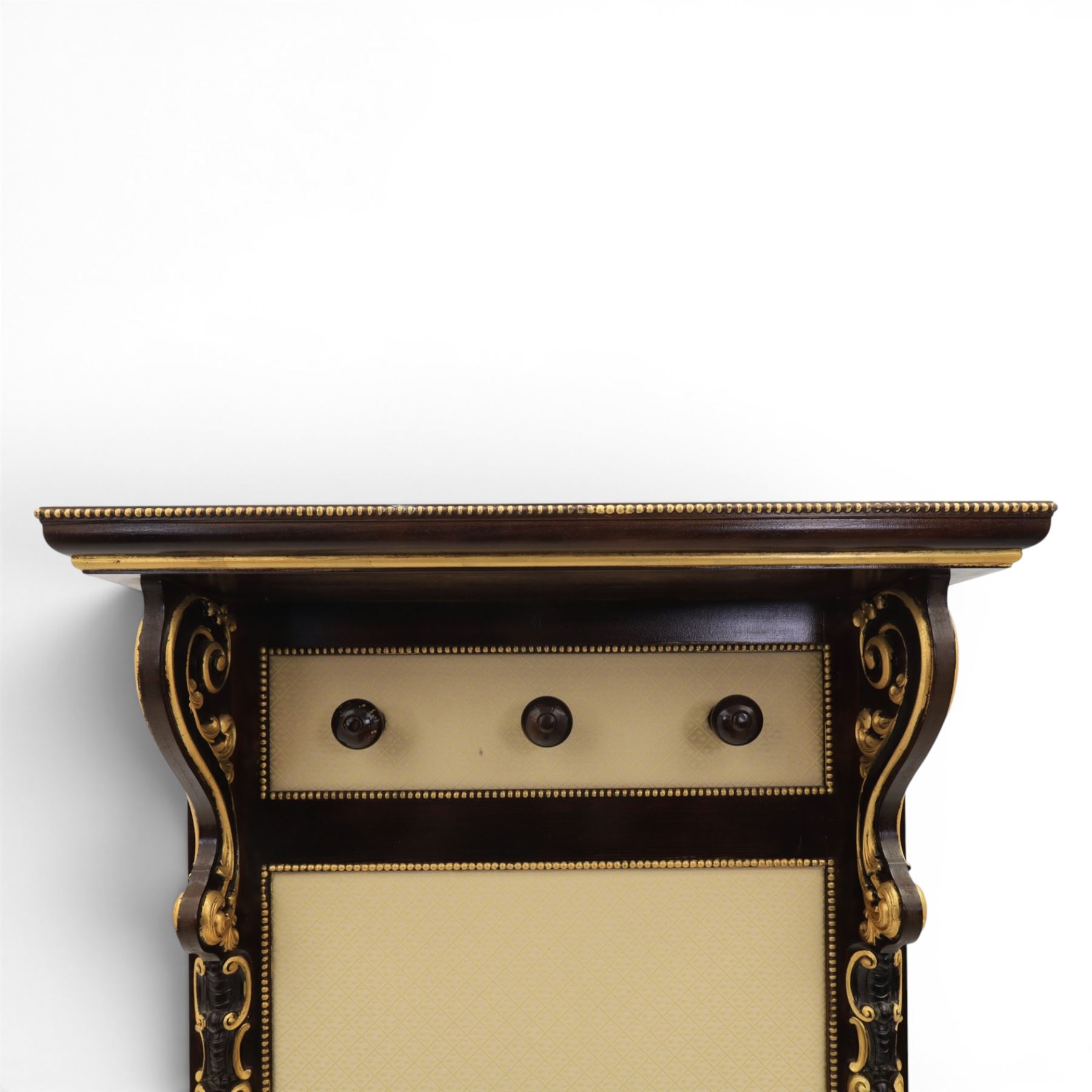 Empire design ebonised and parcel gilt hall stand, projecting moulded cornice with bead and reel border, upper rail fitted with three turned hat and coat pegs, central cream upholstered panel within beaded slip, flanked by scrolled uprights with gilt foliate and anthemion mounts, lower acanthus leaf apron, on paw feet