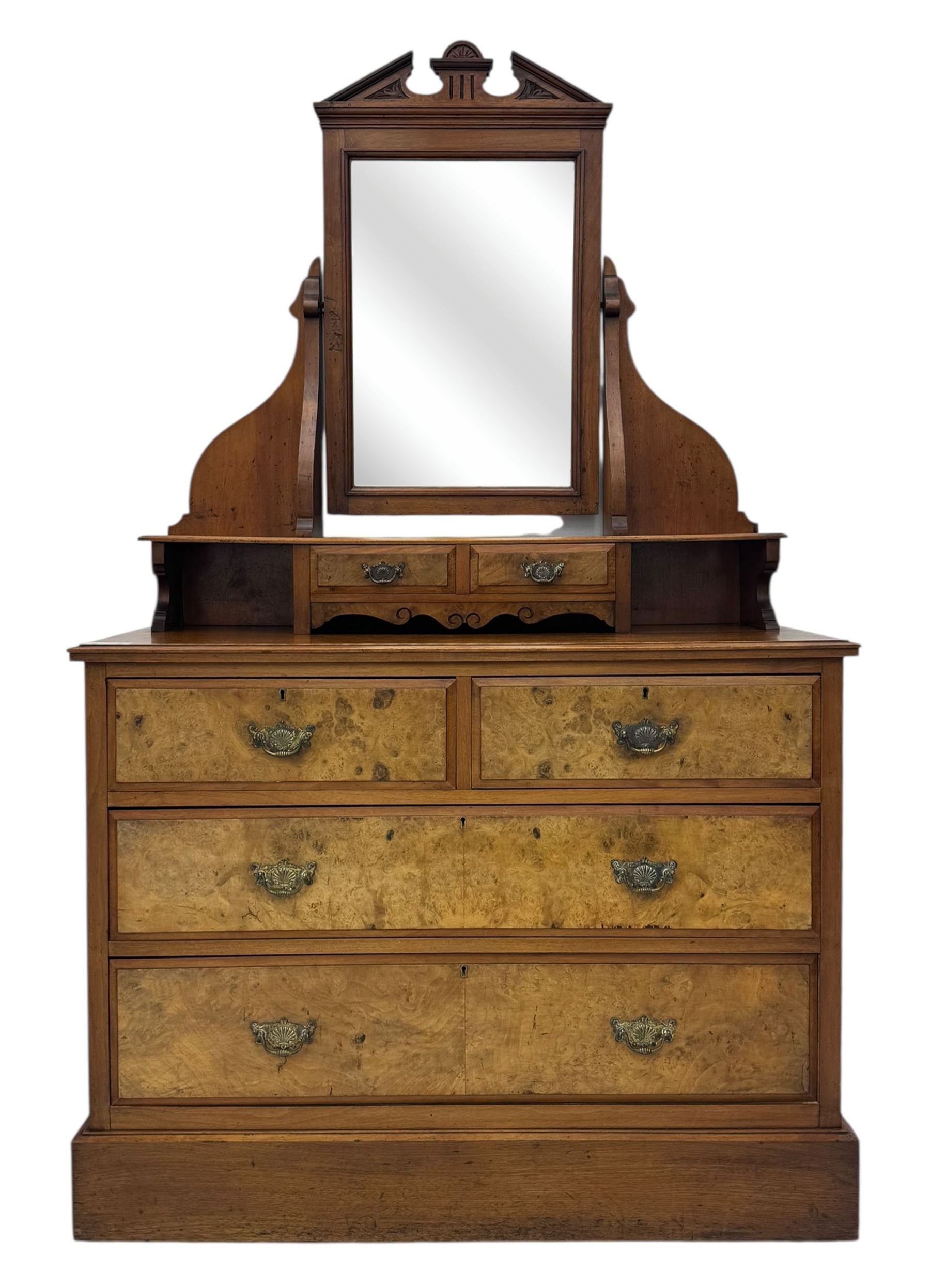 Victorian walnut bedroom suite - wardrobe, dressing chest and bedside cupboard, comprising a full-length wardrobe with broken pediment and central mirrored door, large lower drawer, a matching dressing table with bevelled swing mirror over two trinket drawers and two short drawers over two long drawers, and a single-door bedside cupboard, all with moulded edges, decorative panel work and shaped aprons