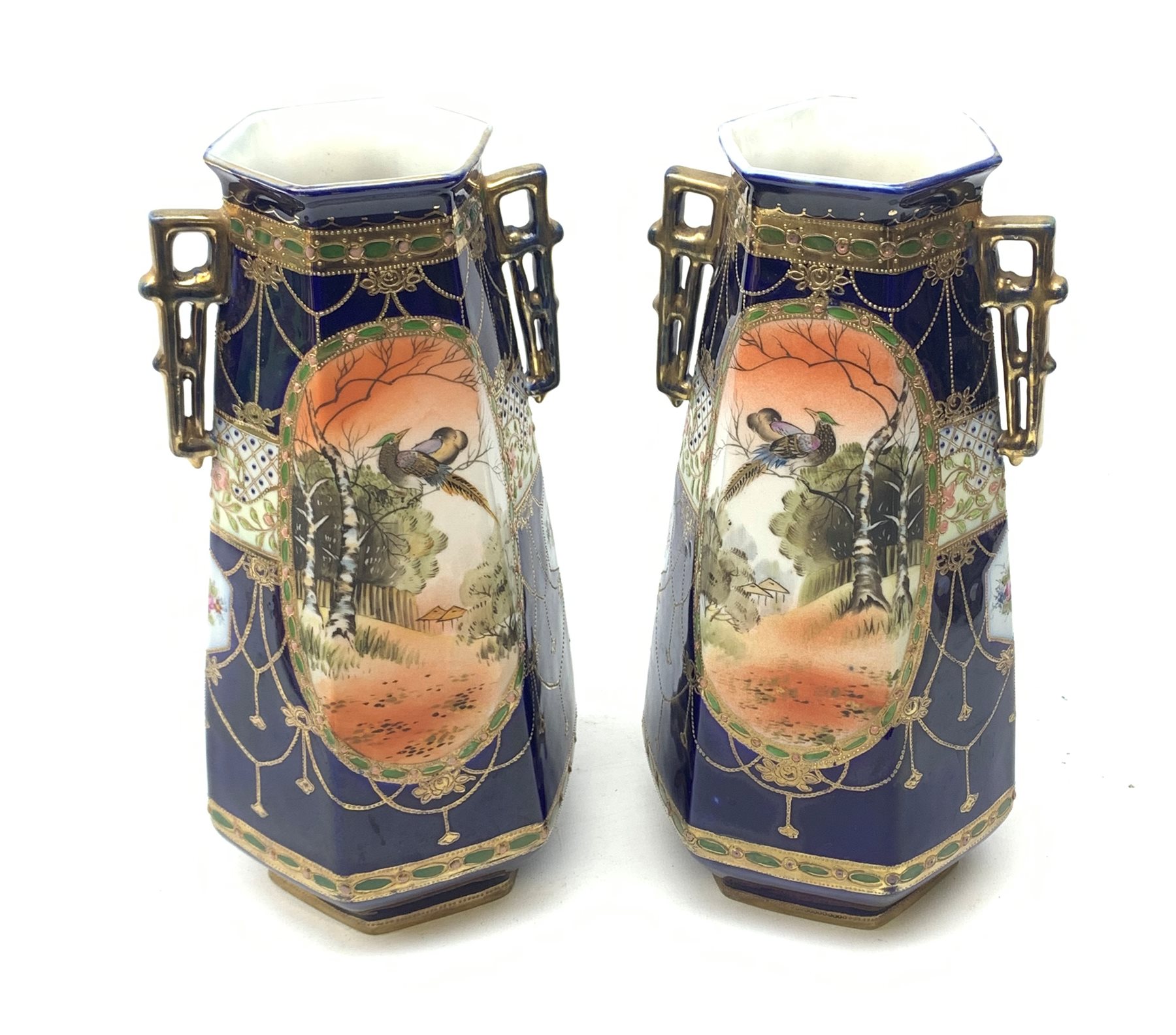 A pair of Japanese Nippon Kinjo vases, of tapering hexagonal form with twin stylised handles, the cobalt blue ground with oval hand painted panels to front and verso depicting landscapes, further detailed with smaller floral bands and panels and heightened with gilt, each with mark beneath, H30.5cm.  