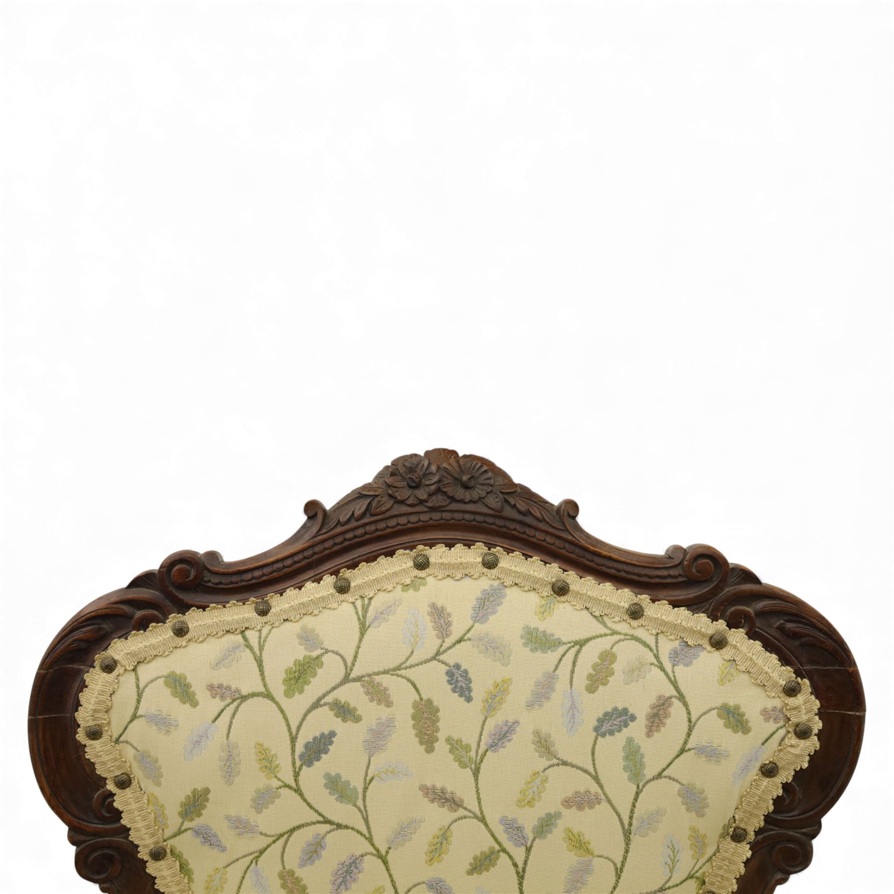 Victorian mahogany framed upholstered armchair, shaped and scroll carved cresting rail above a padded upholstered back with applied braid trim, swept open arms with carved terminals and upholstered arm pads, over a serpentine fronted deep stuffed seat, raised on cabriole forelegs terminating in carved claw feet