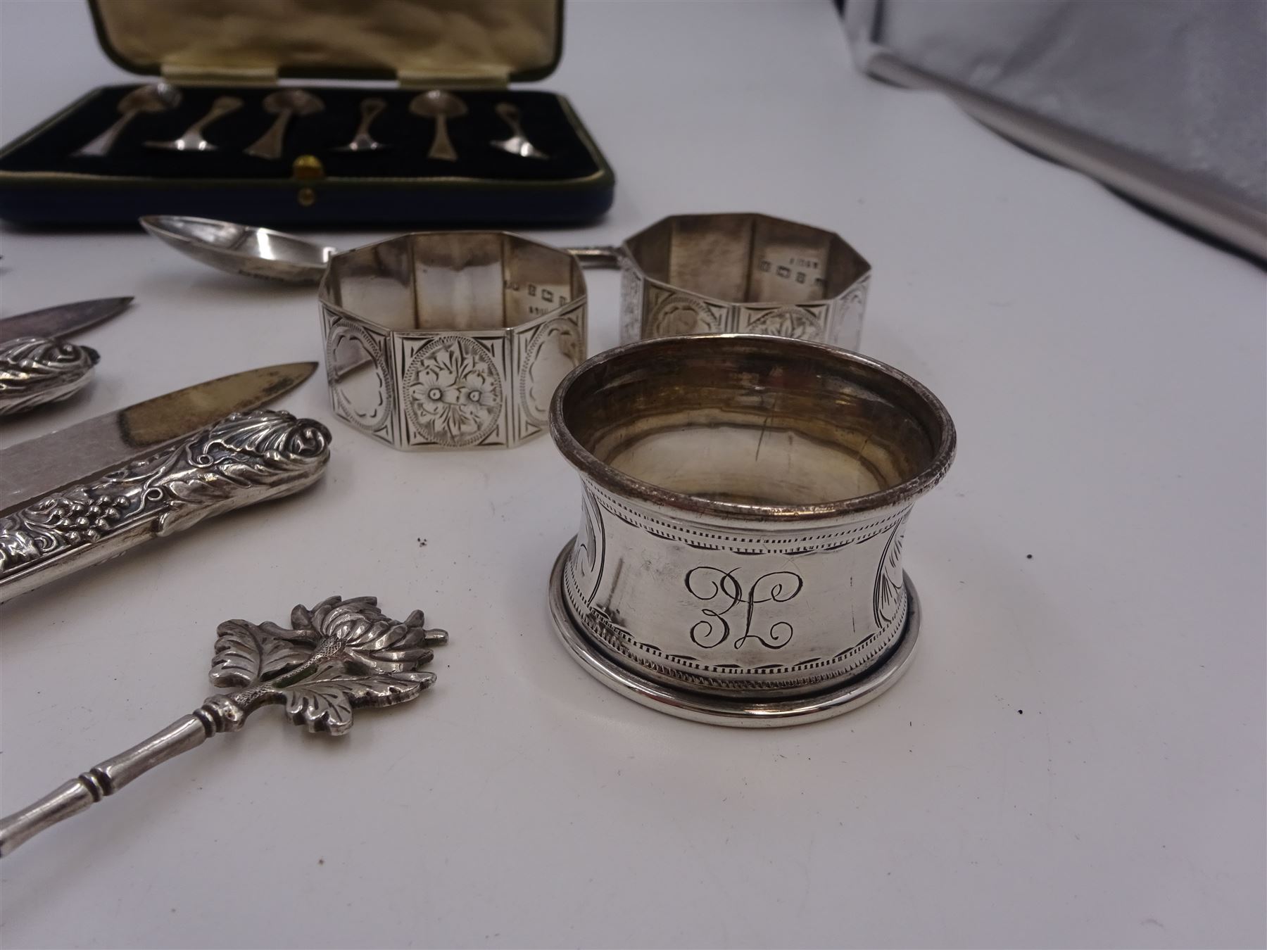 Set of 1930s silver handled fruit knives and forks, for six place settings, the handles decorated in relief with fruiting vines, hallmarked Walker & Hall, Sheffield 1934, together with a set of six 1920s silver egg spoons, with pin prick engraving to handle, hallmarked Thomas Bradbury & Sons Ltd, Sheffield 1929, in fitted case, three silver napkin rings, to include a pair, of octagonal form, with floral engraving, hallmarked John Rose, Birmingham 1951 and two silver souvenir spoons