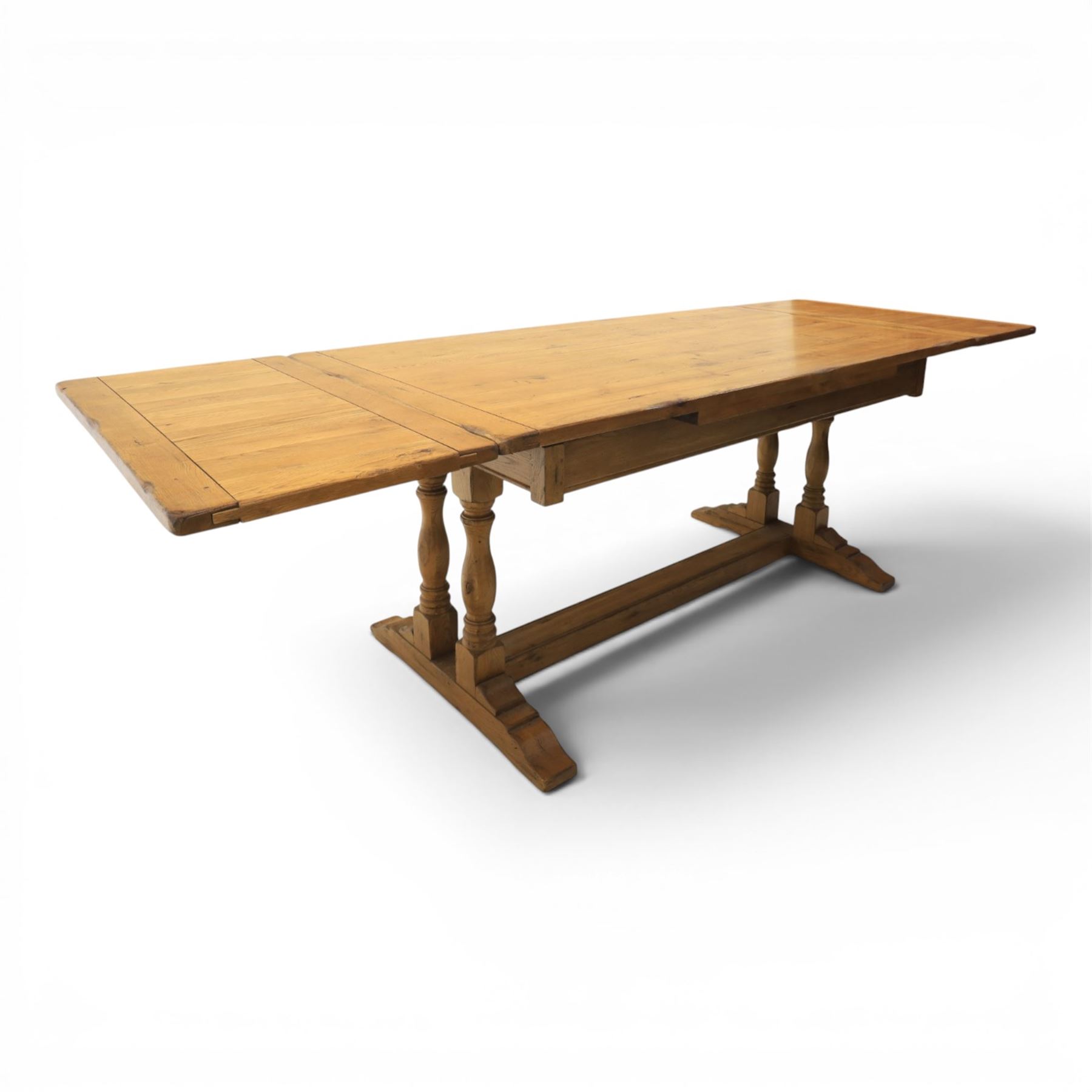 Traditional oak refectory dining table, fitted with draw leaves to either end extending to 257cm, on twin turned and block supports united by a stretcher, terminating in shaped trestle feet