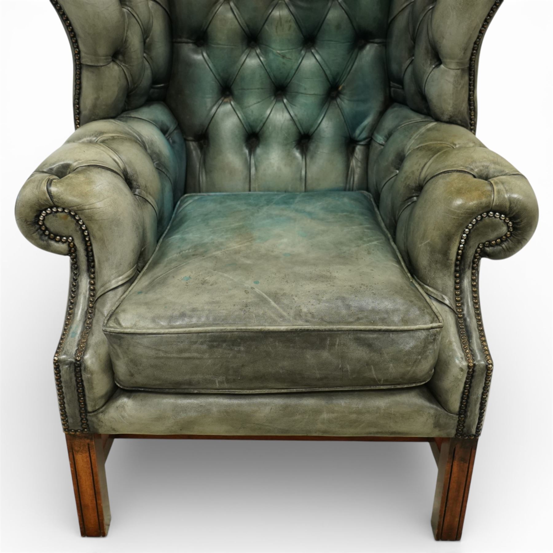 Georgian design mahogany framed wingback armchair, upholstered in rustic pale green buttoned leather with loose seat cushion, raised on square supports united by H-stretcher