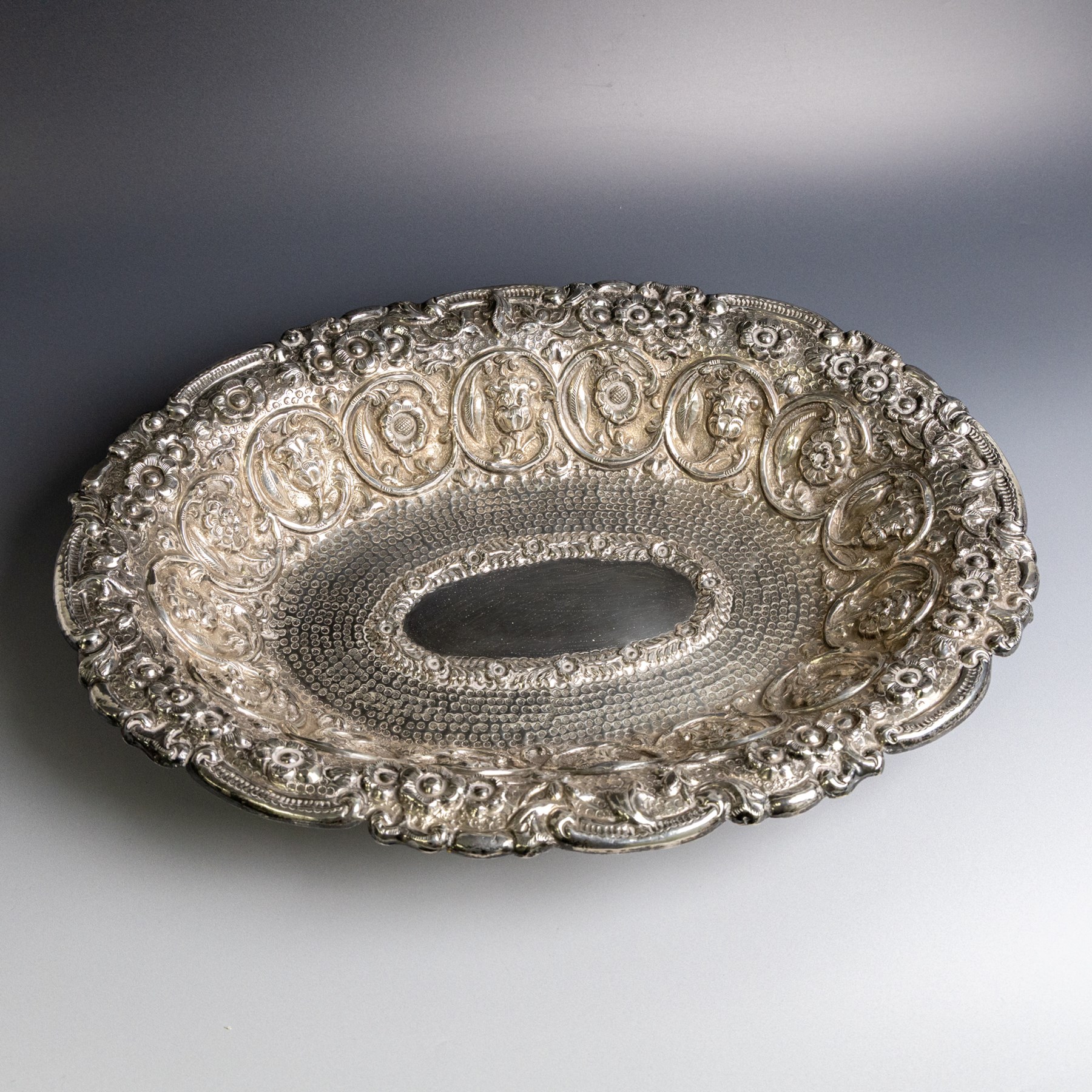 Late 19th/early 20th century continental silver serving bowl, of oval form, profusely embossed with scrolling floral and foliate decoration, with hammered finish to interior