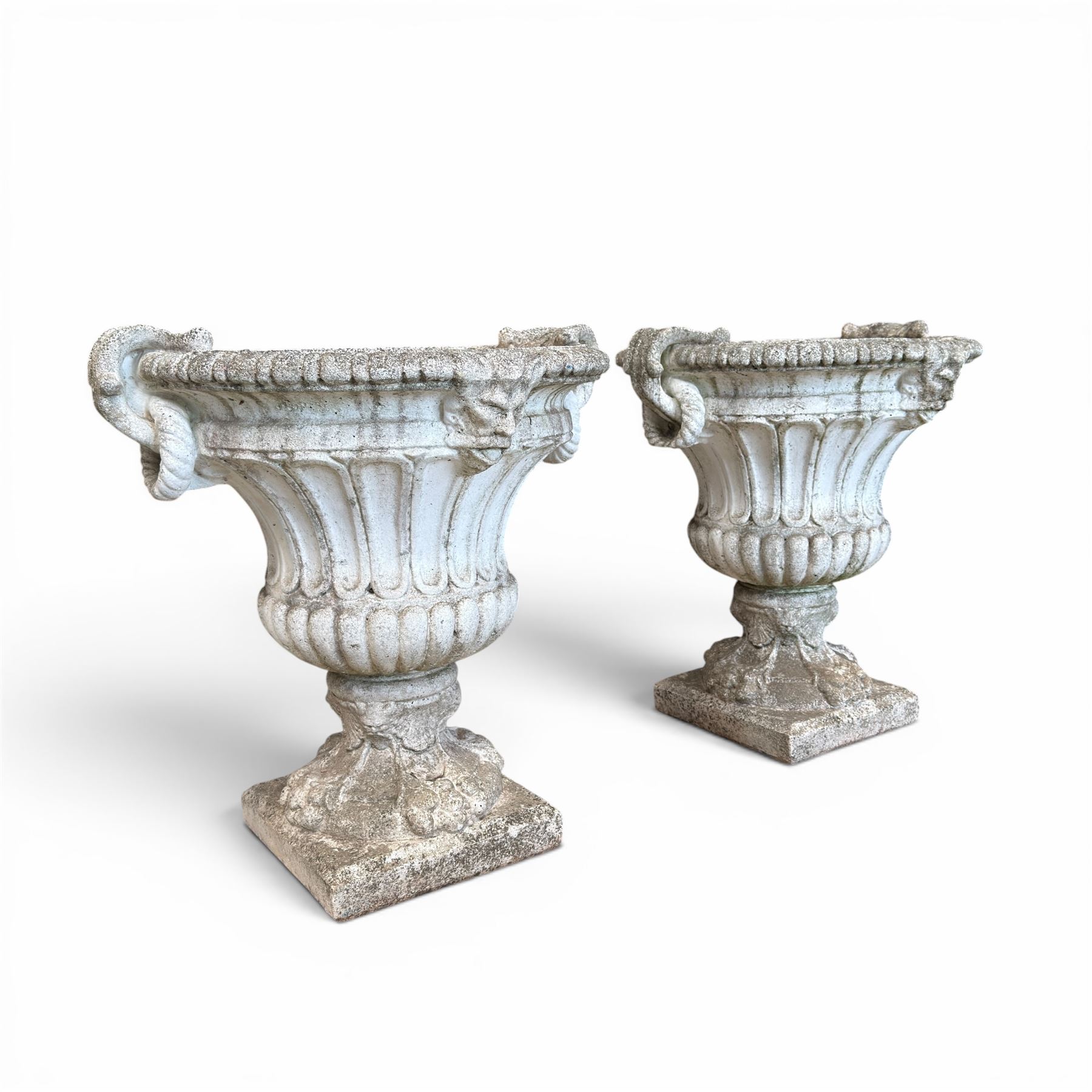Pair of Neoclassical design cast stone garden urns, each of campana form with fluted body and gadrooned underbelly, decorated with faun/satyr opposing masks and ropetwist handles, with floral and mask design to the socles, raised on square bases, finished in weathered white patina