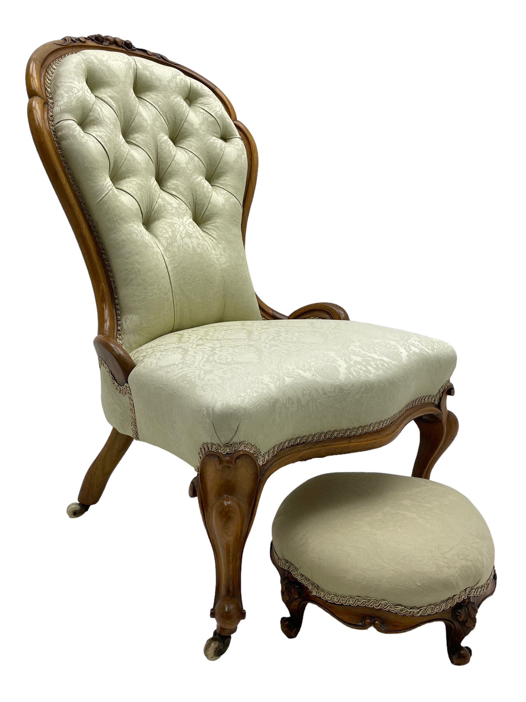 Victorian walnut framed nursing chair, the cresting rail decorated with carved applied flower heads and acanthus leaves, shaped back and sprung seat upholstered in buttoned ivory damask fabric, serpentine front over cartouche carved cabriole supports with ceramic castors (W57cm H92cm); with matched footstool, circular top over shaped moulded apron, on floral carved cabriole feet (W34cm) 