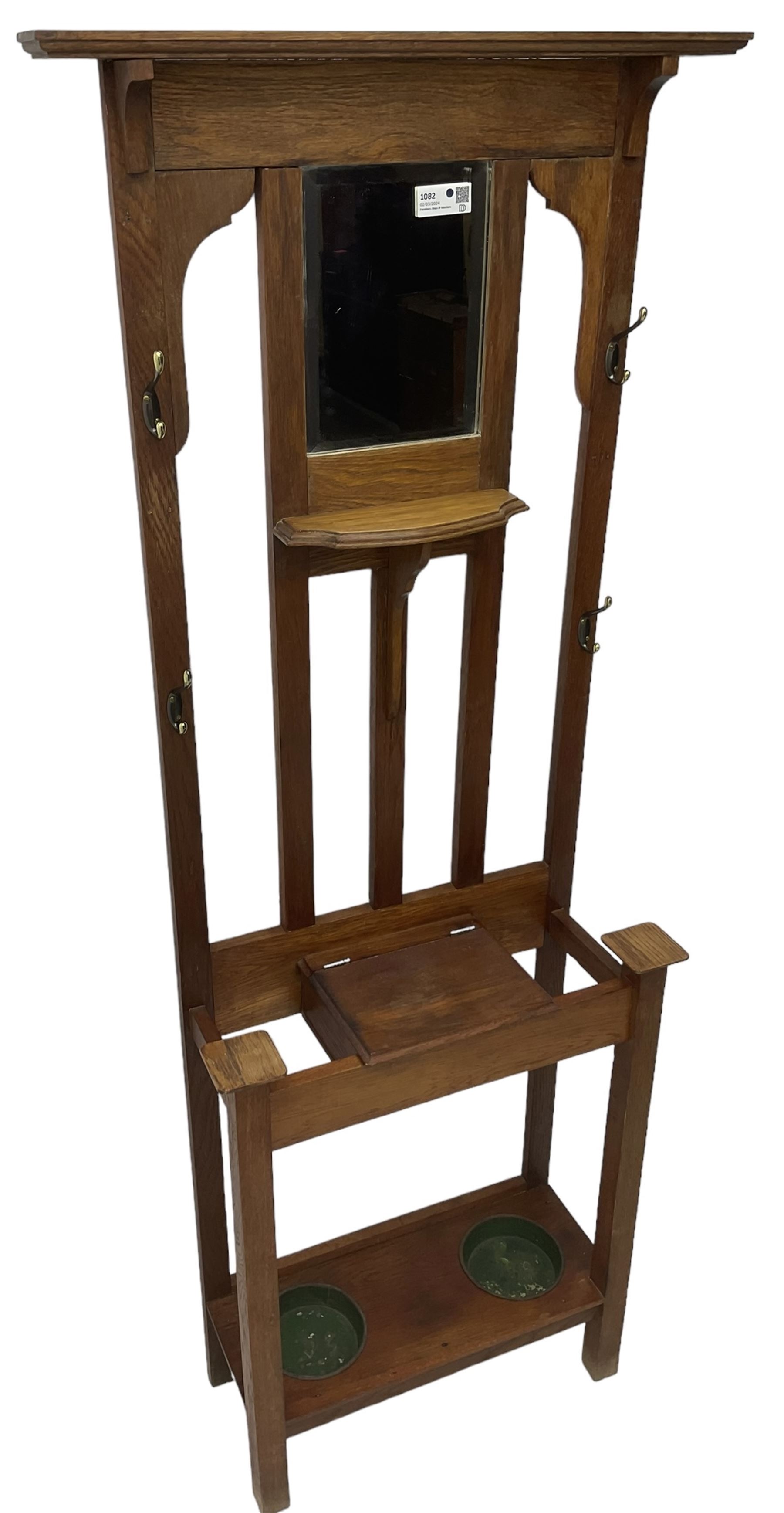 Edwardian oak hall stand, raised back with rectangular bevelled mirror plate surrounded by shelf and coat hooks, fitted with a glove box with hinged lid, over an undertier with two inset umbrella drip trays
