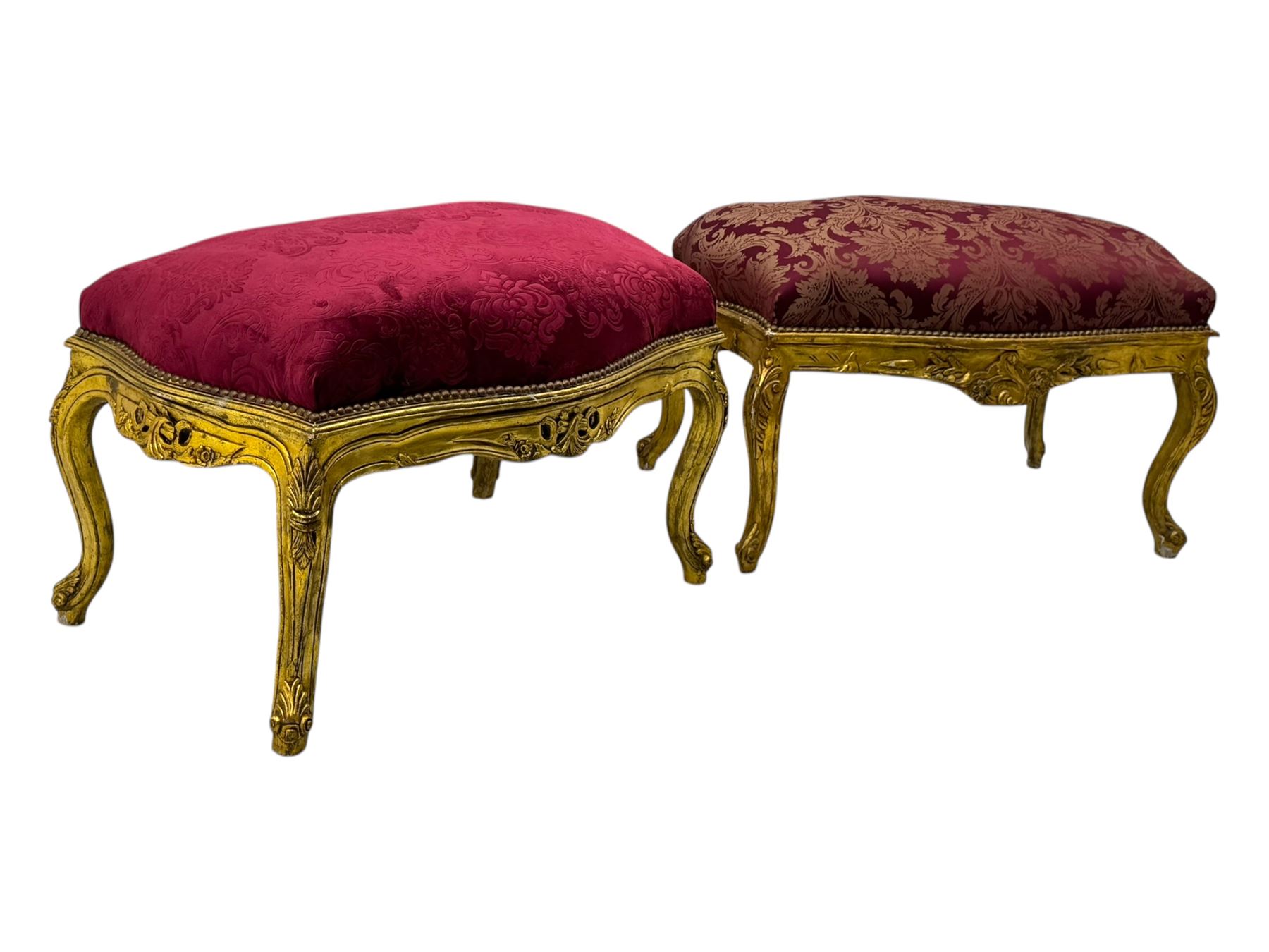 Pair of Louis XV-design giltwood stools, each upholstered in red damask fabric with slight variations in patterns, the carved frames adorned with scrolling foliage and shell motifs, raised on cabriole supports