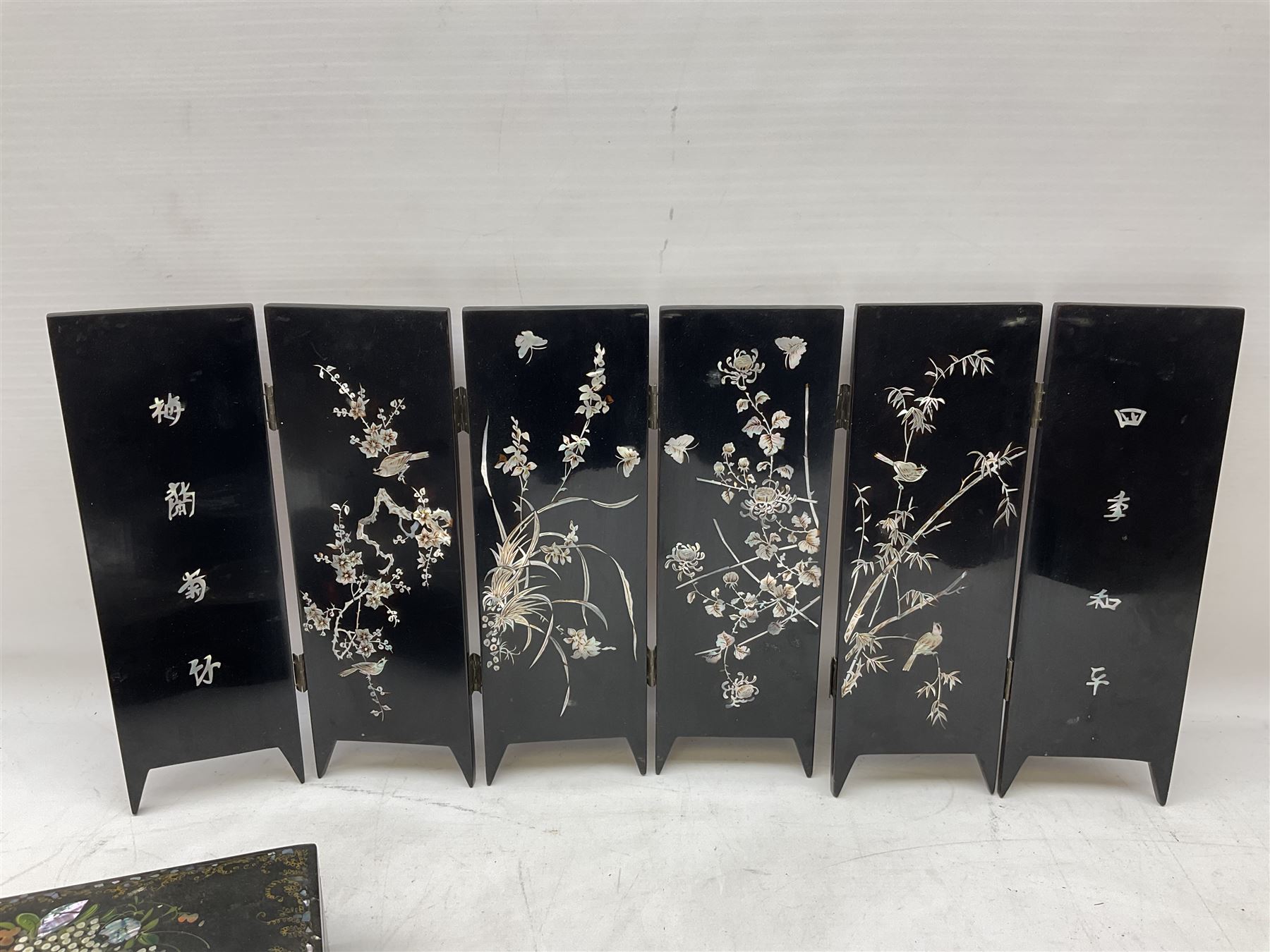  Late 19th / early 20th century Japanese lacquered table top cabinet, heavily decorated with mother of pearl inlay depicting blossoming branches, flowers and birds, the two hinged doors between longer drawers opening to reveal interior fitted with four short drawers, with lift up hinged canted lid, H28cm D9.5cm W23cm, together with mother of pearl inlaid miniature folding screen, dish decorated with walking figures with crimped edge, boxes decorated with flowers, birds and gilt etc