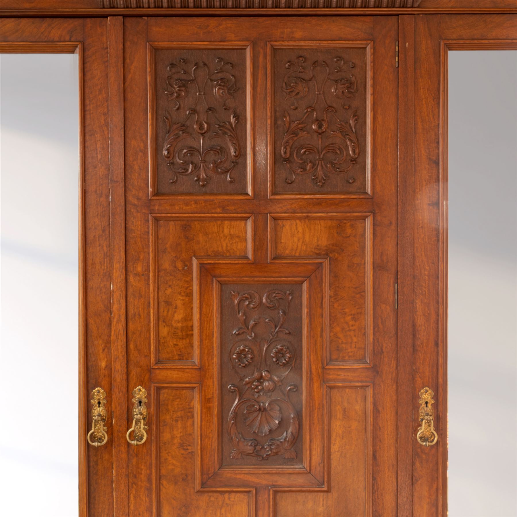 Late Victorian oak and burr oak three-section mirror wardrobe, central door with three carved panels with shell and acanthus decoration, fitted with four drawers and four tray drawers, linen sides with bevelled mirrored panel doors with hanging space, plinth base, and dental cornice