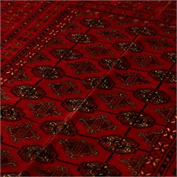 Turkman hand-knotted carpet, deep red ground, with an all-over field of repeating gul motifs arranged in rows, enclosed by multiple red geometric borders with stylised flowerheads and hooked motifs, flanked by narrow patterned guard stripes, with wool fringes