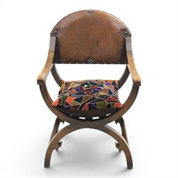 Early 20th century mahogany Savonarola chair, arched leather back with brass studwork, curved open arms with incised geometric decoration, loose patchwork velvet cushion seat, X-frame supports united by circular side rails, on scrolled feet