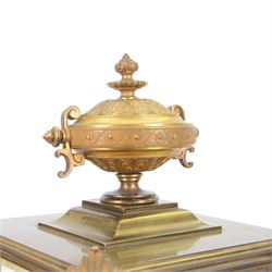 French- Art-deco Edwardian 8-day four-glass clock garniture, with etched glass panels, cast brass decoration to the corners of the case and splayed feet representing cloven hoofs to the base, case surmounted by a large oval urn on a tiered brass platform, two part dial with a recessed brass centre comprising of pierced radial decoration, with steel spade hands and Arabic numerals to the chapter, rack striking movement with a deadbeat Brocot escapement, striking the hours and half-hours on a bell. With a visible twin file mercury pendulum. Garni comprising two large twin handled urns on rectangular pedestals raised on conforming feet representing cloven hoofs, Clock and garni presented on three shaped wooden gesso bases with velvet pads. With key.