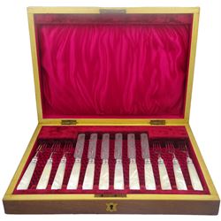Edwardian mother of pearl handled dessert forks and knives with silver ferrules, prongs and foliate engraved blades, for six place settings, hallmarked John Henry Potter, Sheffield 1905, contained within a mahogany case with vacant brass cartouche to the hinged cover, opening to reveal a red silk and velvet lined interior, 

