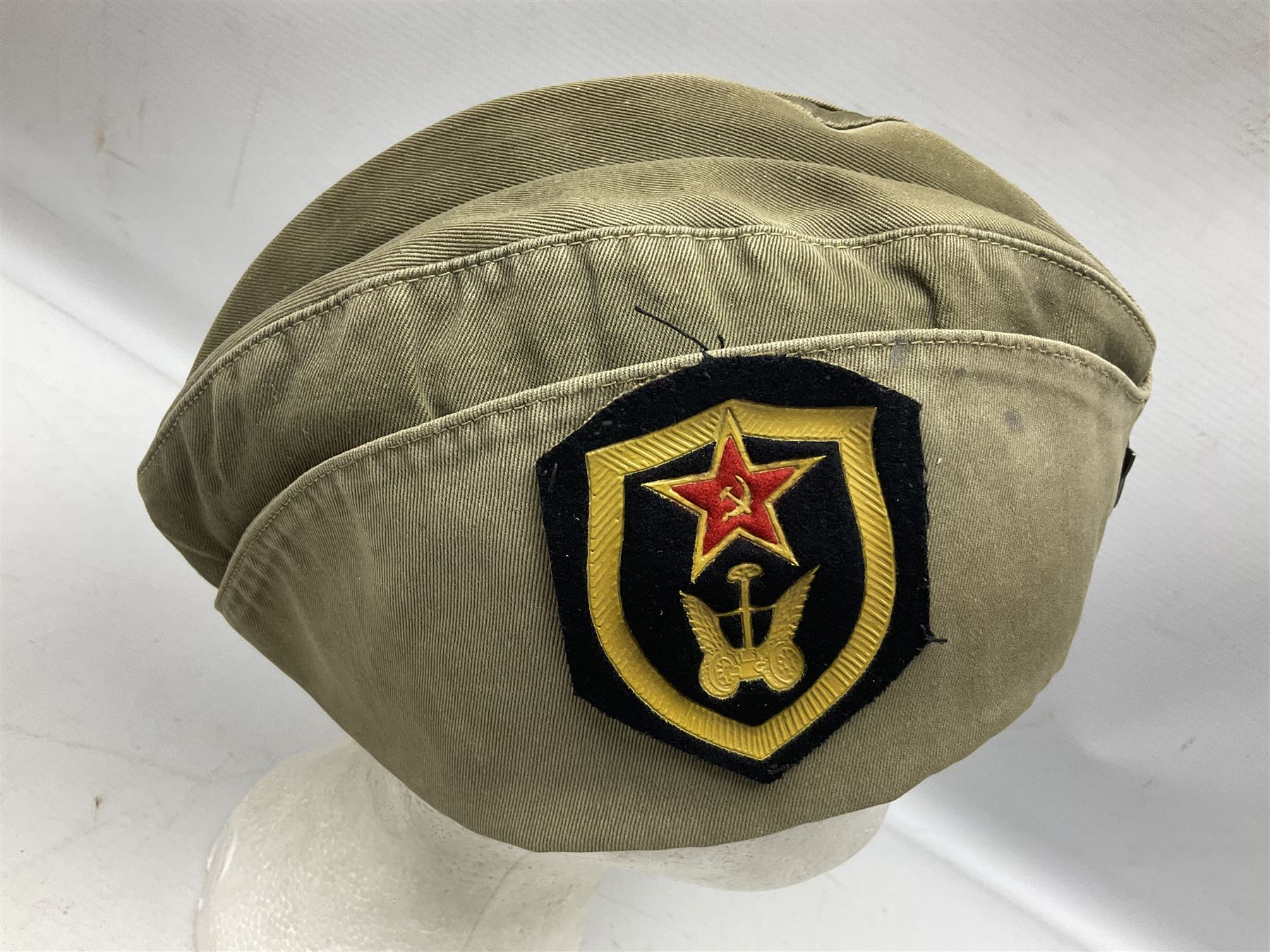 Four side caps - WW2 Russian, post-WW2 Russian and two East German; all with badges, one with multiple metal badges (4)