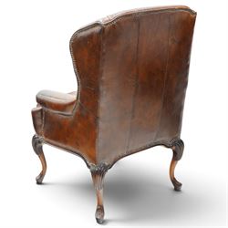 Pair of quality Queen Anne design mahogany framed wingback armchairs with matching footstools, the high sprung winged backs over rolled arms with studwork, raised on elegant reeded scroll carved cabriole supports, upholstered in deep chocolate brown leather (W82cm D75cm H112cm), the footstools with ovoid padded seat over studwork and moulded lower rail and cabriole supports (W65cm D42cm H48cm)