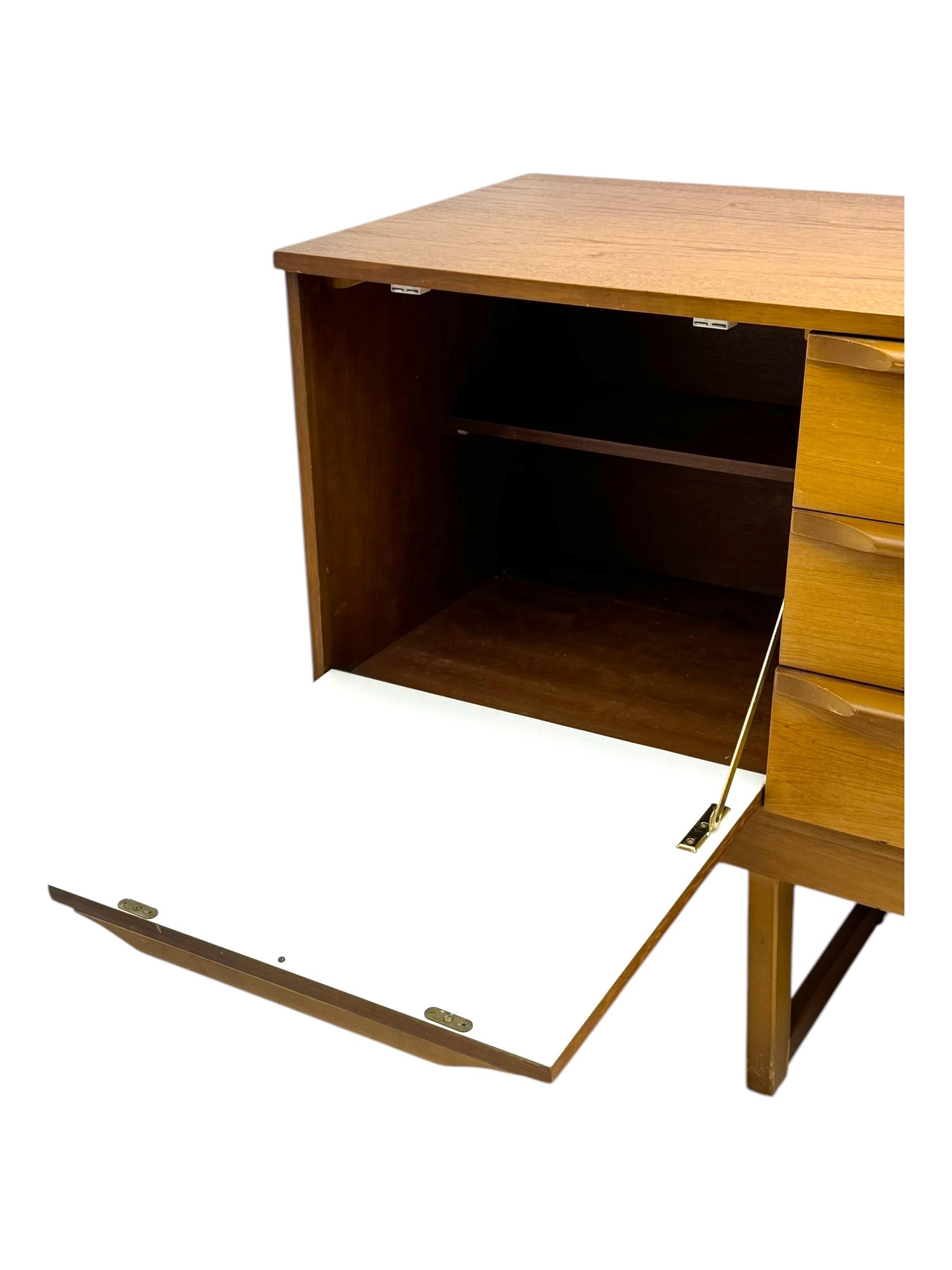 Mid-20th century teak sideboard, fitted with a fall-front cupboard, three drawers including a green baize-lined cutlery drawer, and a double cupboard, with integrated handles, on sleigh supports