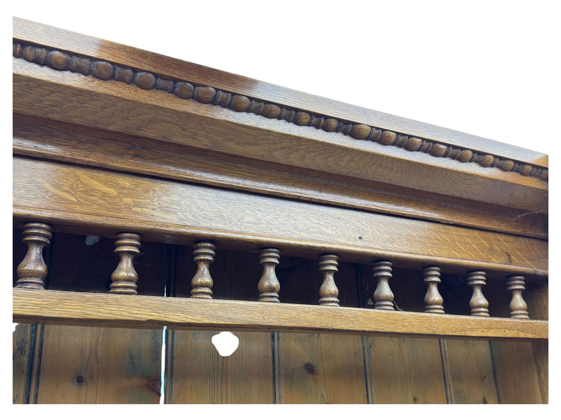 Late 19th century pine dresser, the projecting cornice with dentil and spindle moulded frieze above a three-tier plate shelves, flanked by glazed doors, the base fitted with three frieze drawers over arched apron and carved floral panelled cupboard doors, raised on turned feet