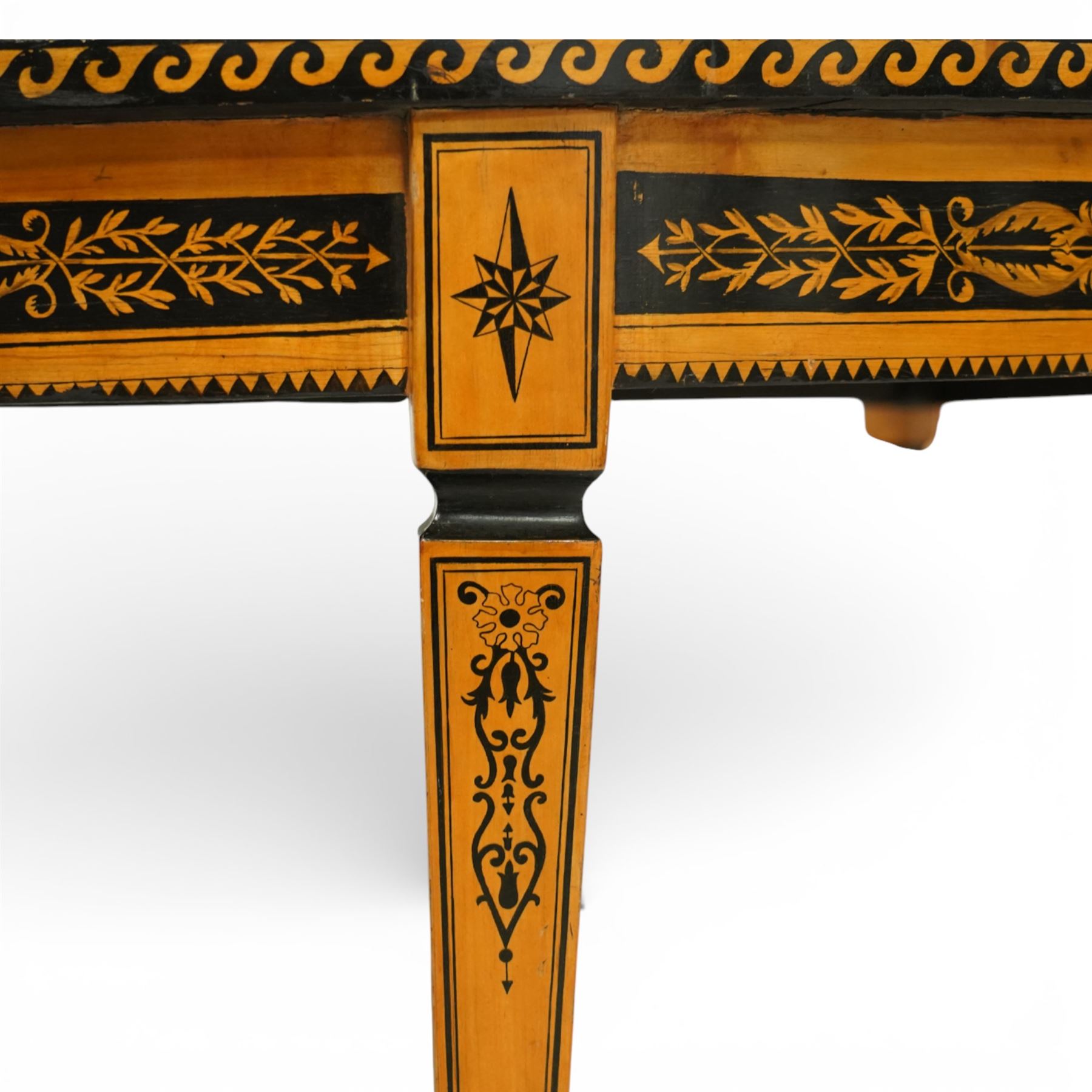 20th-Century Louis XVI-Style satinwood and penwork circular table or pair of console tables, the circular quarter-veneered top decorated in penwork with a central classical mask head motif within scrolling foliate and anthemion ornament on a contrasting black ground, above a conforming frieze decorated with Greek key-type scrolls. Raised on square tapering legs, each with an upper block panel decorated with compass-star motifs.