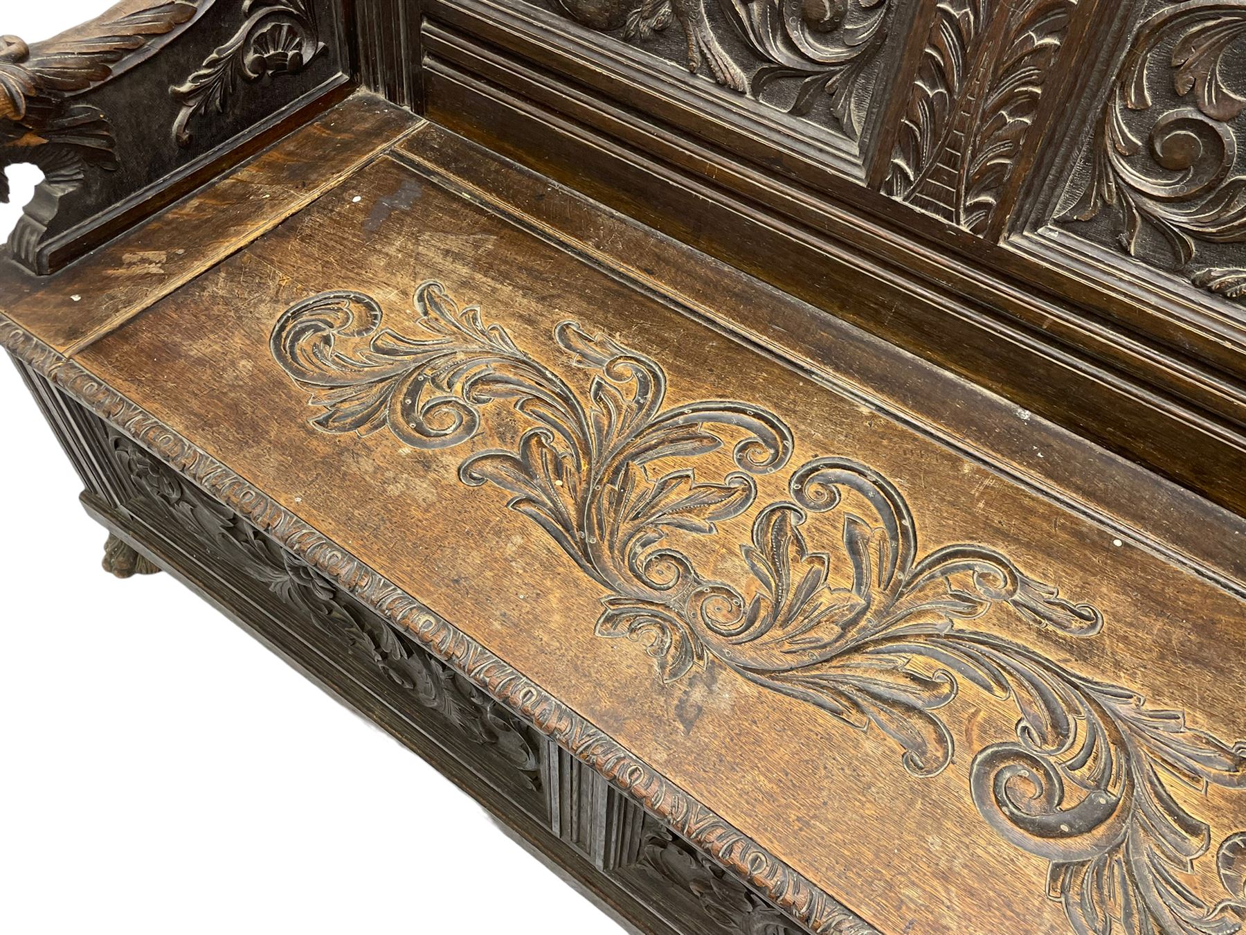 19th century oak hall bench, dentil cresting rail over moulded frame with panelled back carved with fire-breathing mythical beasts and central acanthus leaf motif, scroll carved down-sweeping arms carved with grotesque masks with scrolled foliage and shells, hinged box seat carved with scrolling foliage over panelled front with further carved foliage decoration, on paw carved front feet 