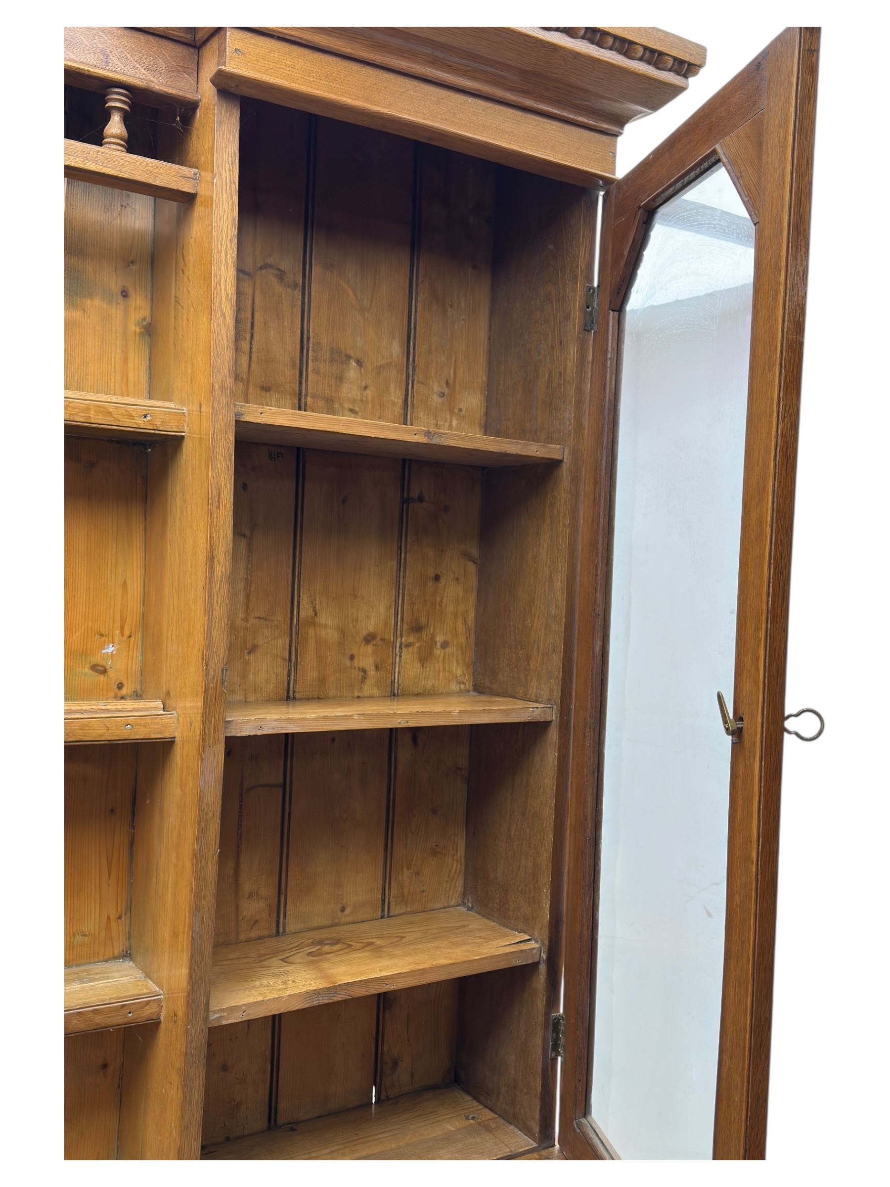 Late 19th century pine dresser, the projecting cornice with dentil and spindle moulded frieze above a three-tier plate shelves, flanked by glazed doors, the base fitted with three frieze drawers over arched apron and carved floral panelled cupboard doors, raised on turned feet
