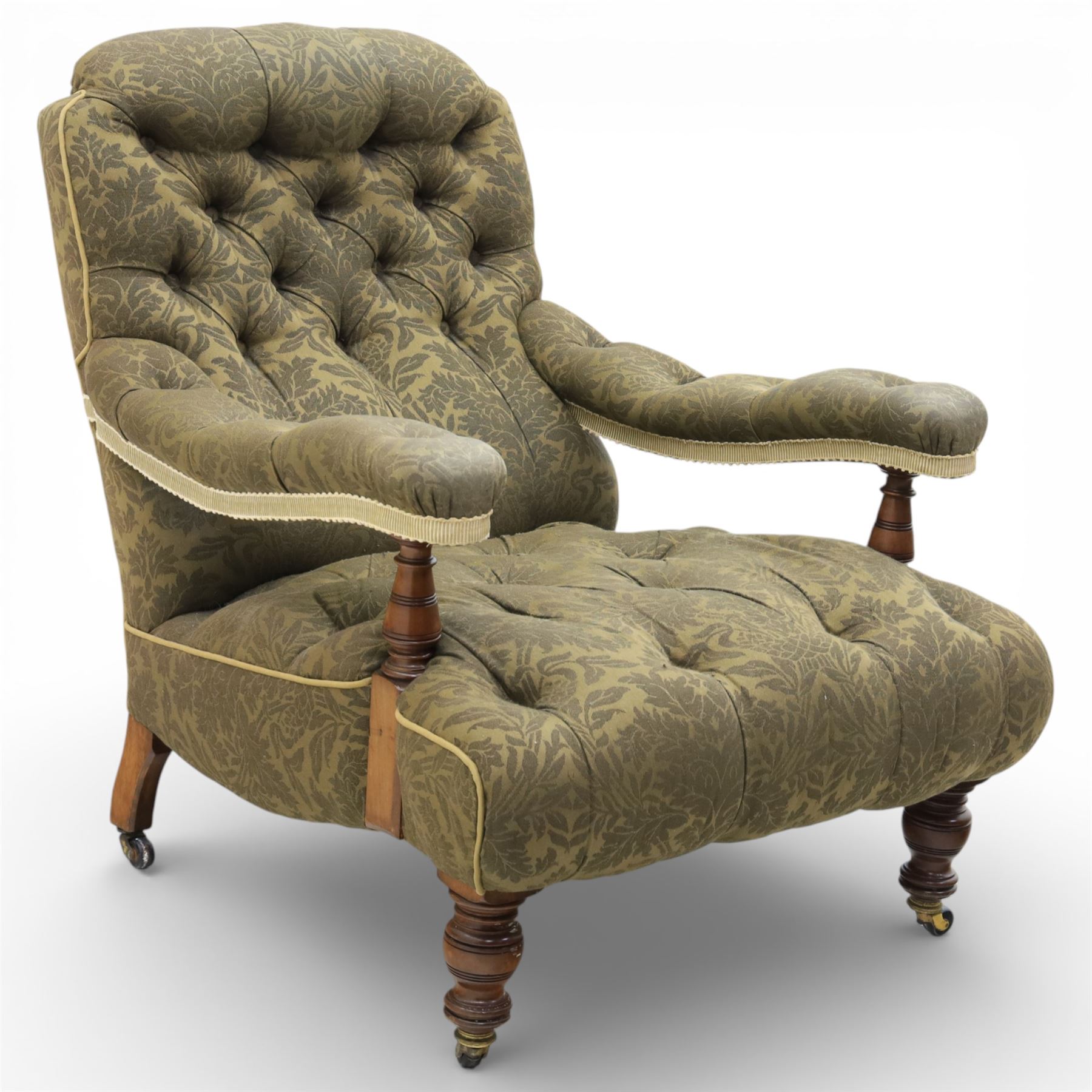 Late Victorian open armchair, in the manner of Howard & Sons, with deep buttoned seat and back upholstered in green damask fabric, with fringed detail to the lower arms, raised upon turned front legs with brass castors