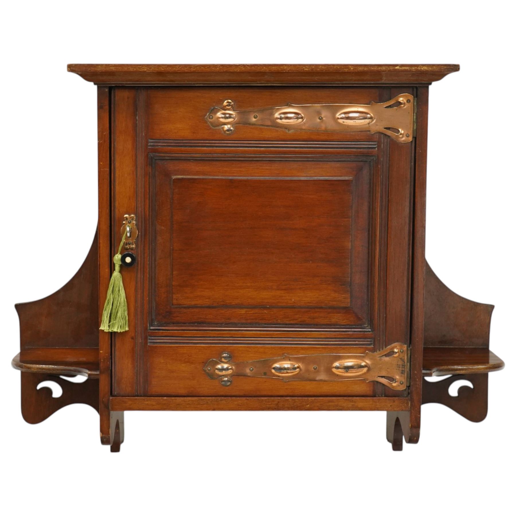 Small Arts & Crafts mahogany wall cupboard, single panelled door enclosing shelf, flanked by two shelves with pierced brackets, with shaped copper fittings and escutcheon 