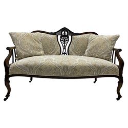 Late Victorian mahogany framed two-seat salon settee, shaped cresting rail pierced and carved with foliate decoration and C-scrolls, upholstered in pale fabric with foliate pattern decorated with stylised plant motifs, shaped and scroll carved arms terminating to shell carved cabriole feet, on brass and ceramic castors