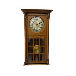 A 1930’s German eight-day spring driven wall clock by Philipp Hass & Sohne striking the hours and half hours on a gong, with an eight-inch silvered dial with a spun brass bezel, Arabic numerals, minute track and steel spade hands, in a flat-topped oak case with full length door and applied mouldings, nine glazed panels with a visible spun brass pendulum. With key.                                   