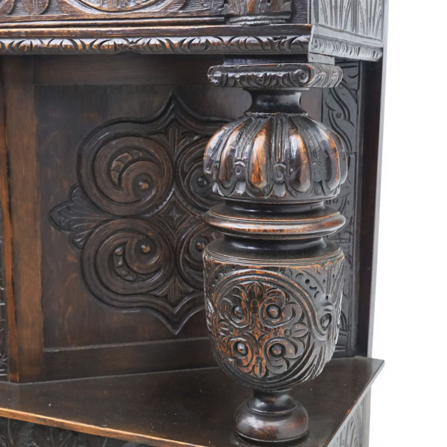 Jacobean revival oak side cabinet, rectangular top above carved frieze of stylised foliage and lunettes, fitted with a central cupboard doors with applied carved panels, above a frieze drawer, supported on turned and carved vase-shaped supports, united by stretcher tier and lower shelf