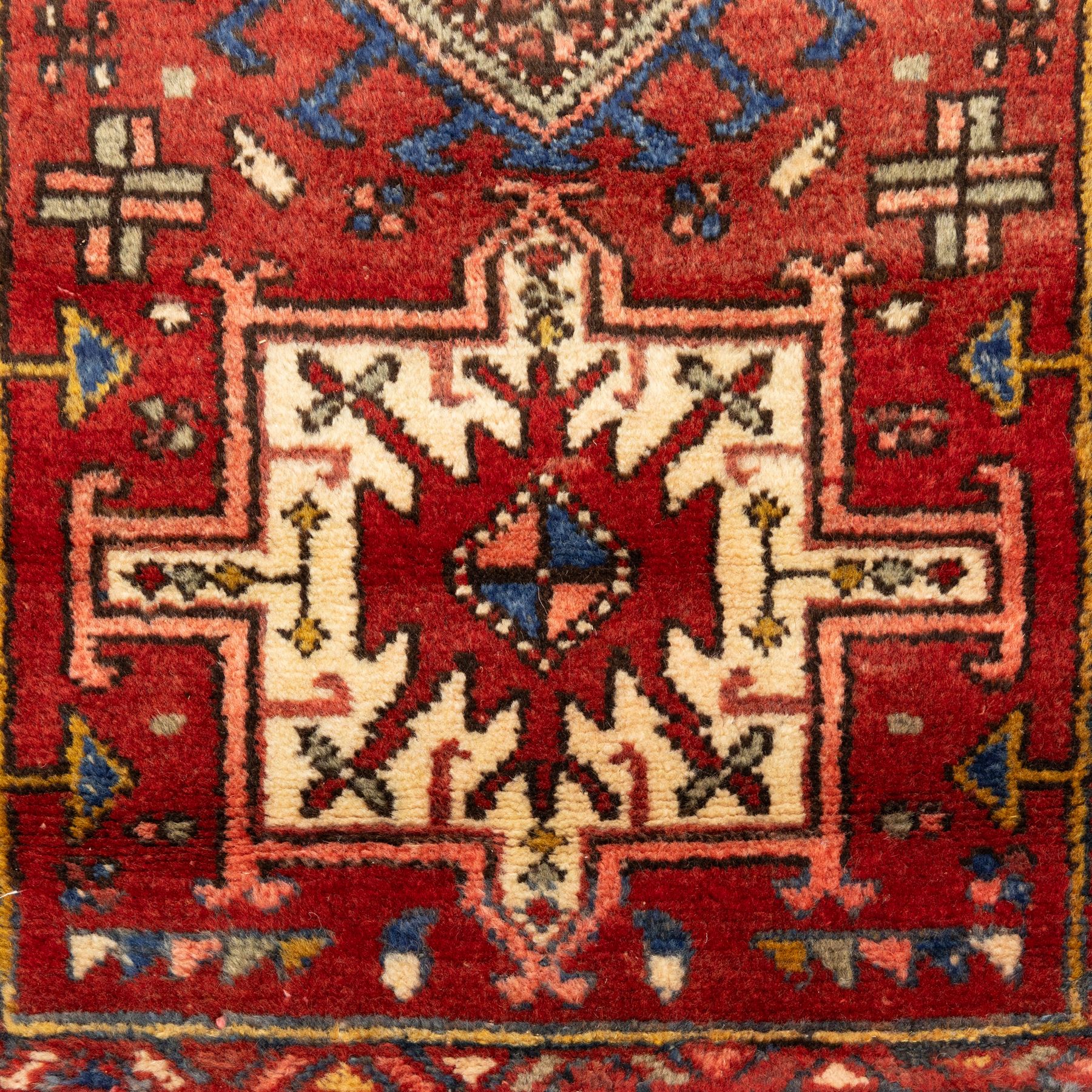 North west Persian Heriz runner, madder red field with a single column of alternating hooked and stepped lozenge medallions in ivory, blue, and terracotta, scattered with small cruciform and geometric motifs within a brick red border, angular motifs between narrow guard stripes 
