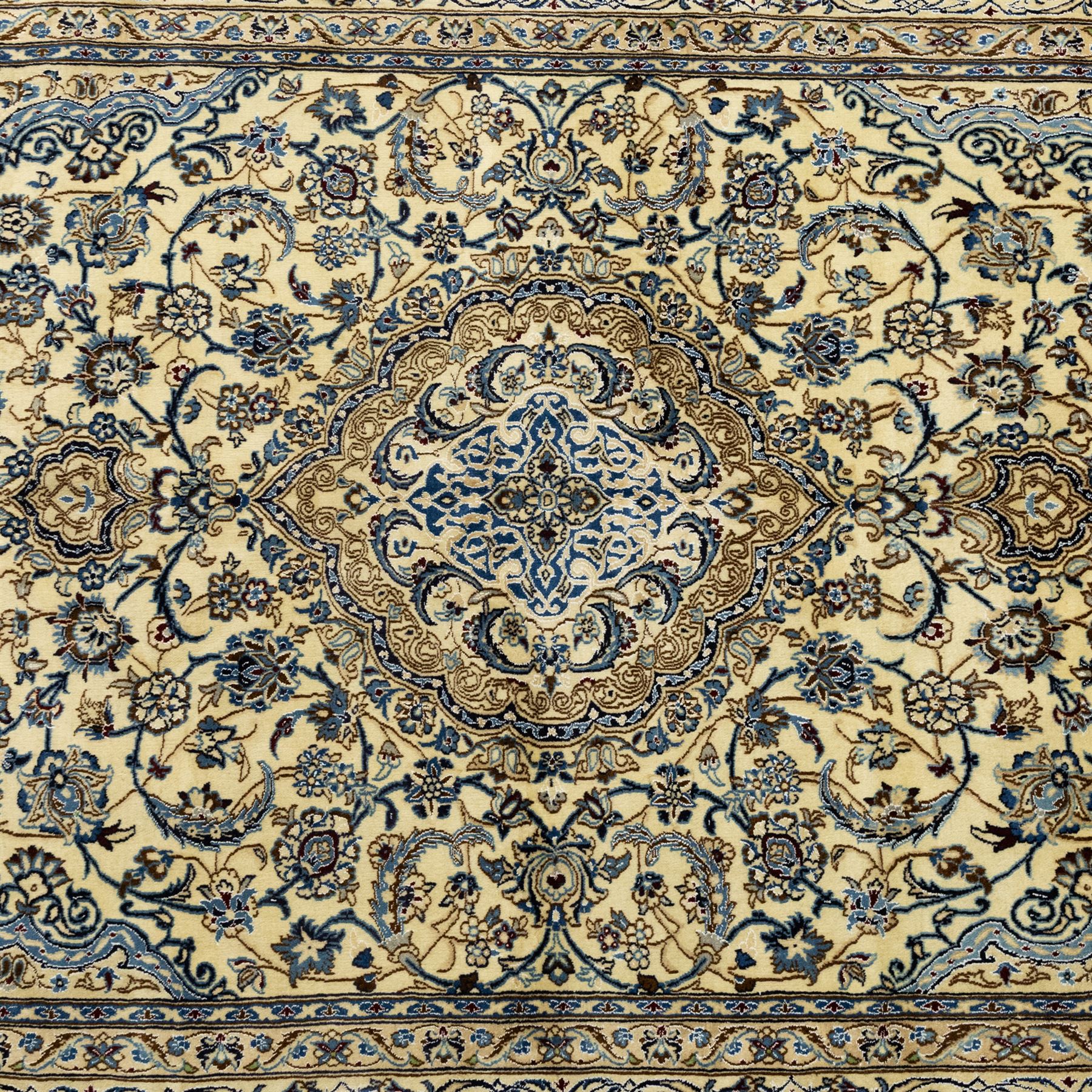 Central Persian Nain hand-knotted carpet, ivory ground, with silk highlights, centred by a shaped floral medallion with pendants, surrounded by scrolling foliate and floral motifs incorporating rosettes, palmettes and delicate vine work in blue, cream and beige tones, enclosed by blue spandrels and an ivory border with repeating palmettes and meandering vines, flanked by floral guard stripes, with cotton fringes