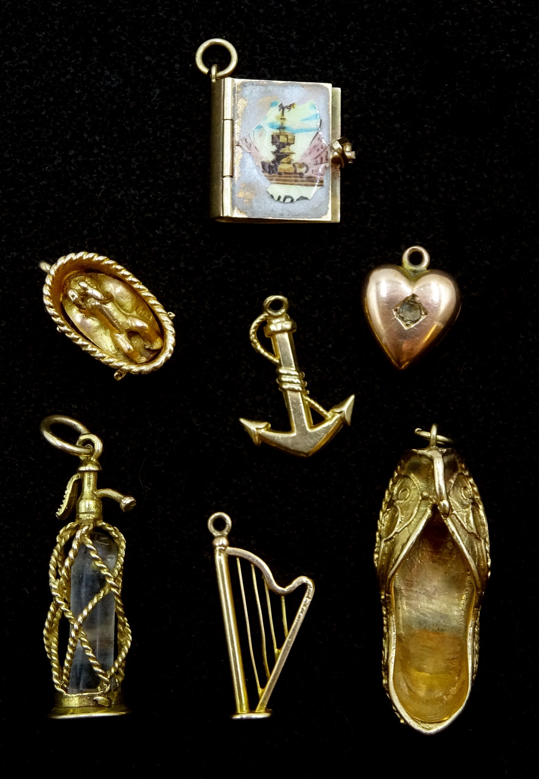 Seven 9ct gold charms including a soda siphon, baby in a basket, harp, Indian shoe and a book, hallmarked or tested