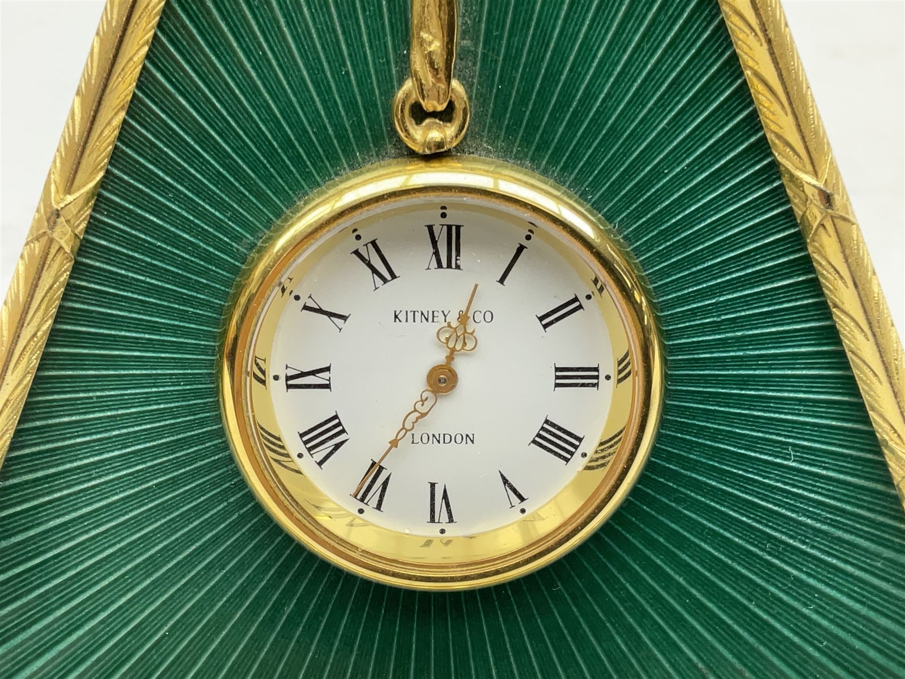 Kitney & Co small desk clock, in green guilloche enamel case of triangular form, decorated with gilt throughout, raised upon two bun feet, H12cm