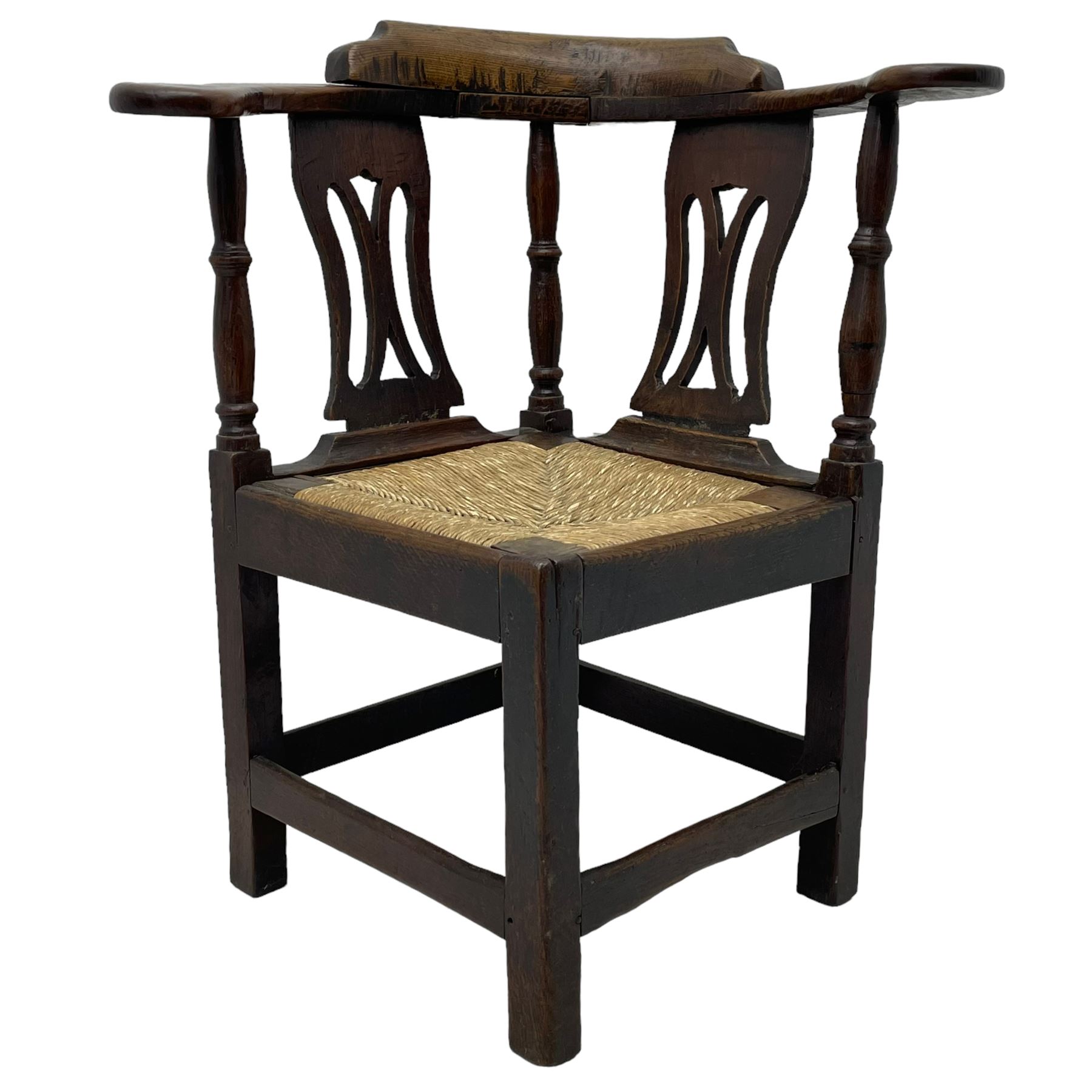 18th century country elm and oak corner chair, the shaped cresting rail terminating to swept arm resets, supported by turned columns and pierced shaped splats, over a drop-in rush seat, raised on square supports united by box stretcher