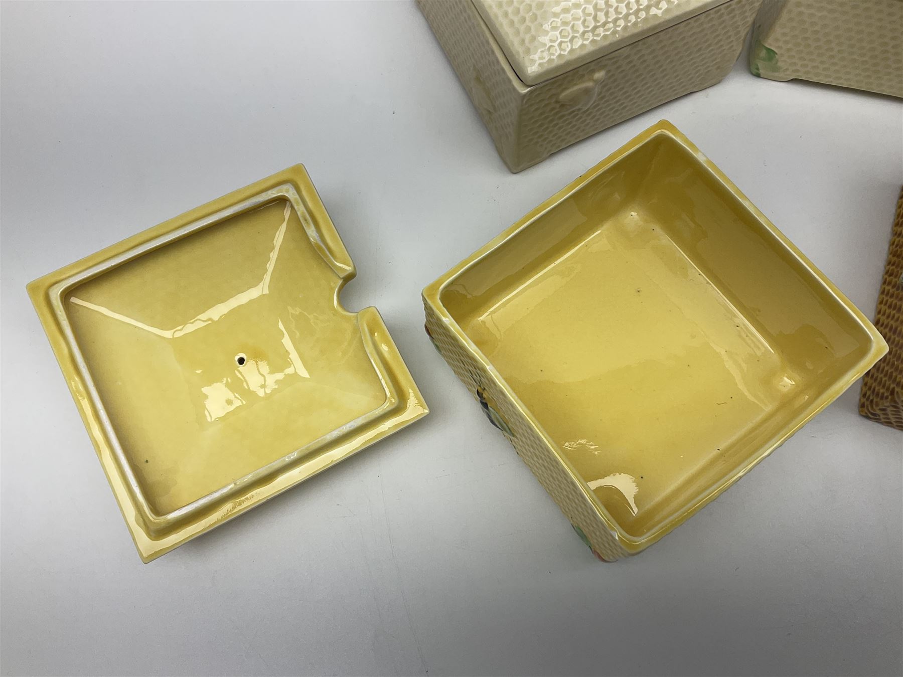 Four square honey boxes with lids,  each decorated with honeycomb pattern and finished with a bee finial