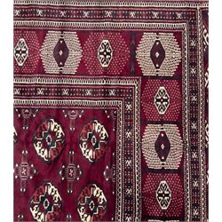 Northeastern Persian Yamut  hand-knotted carpet, the rich burgundy field with repeating rows of stepped gul motifs in cream and black, enclosed by multiple linear and geometric borders with hooked motifs and diamond medallions