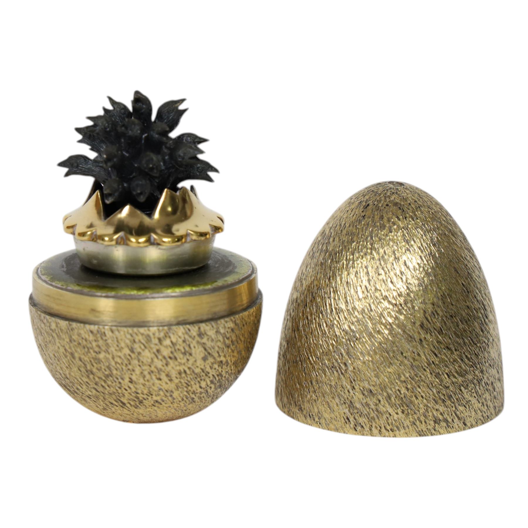 Late 20th century silver and silver-gilt surprise egg, the textured gilt exterior opening to reveal a clutch of chicks, the clustered heads supported upon a spring, within a jagged and lobed silver and gilt encasement, with green enamel surround, hallmarked Stuart Devlin, London 1982, H7cm