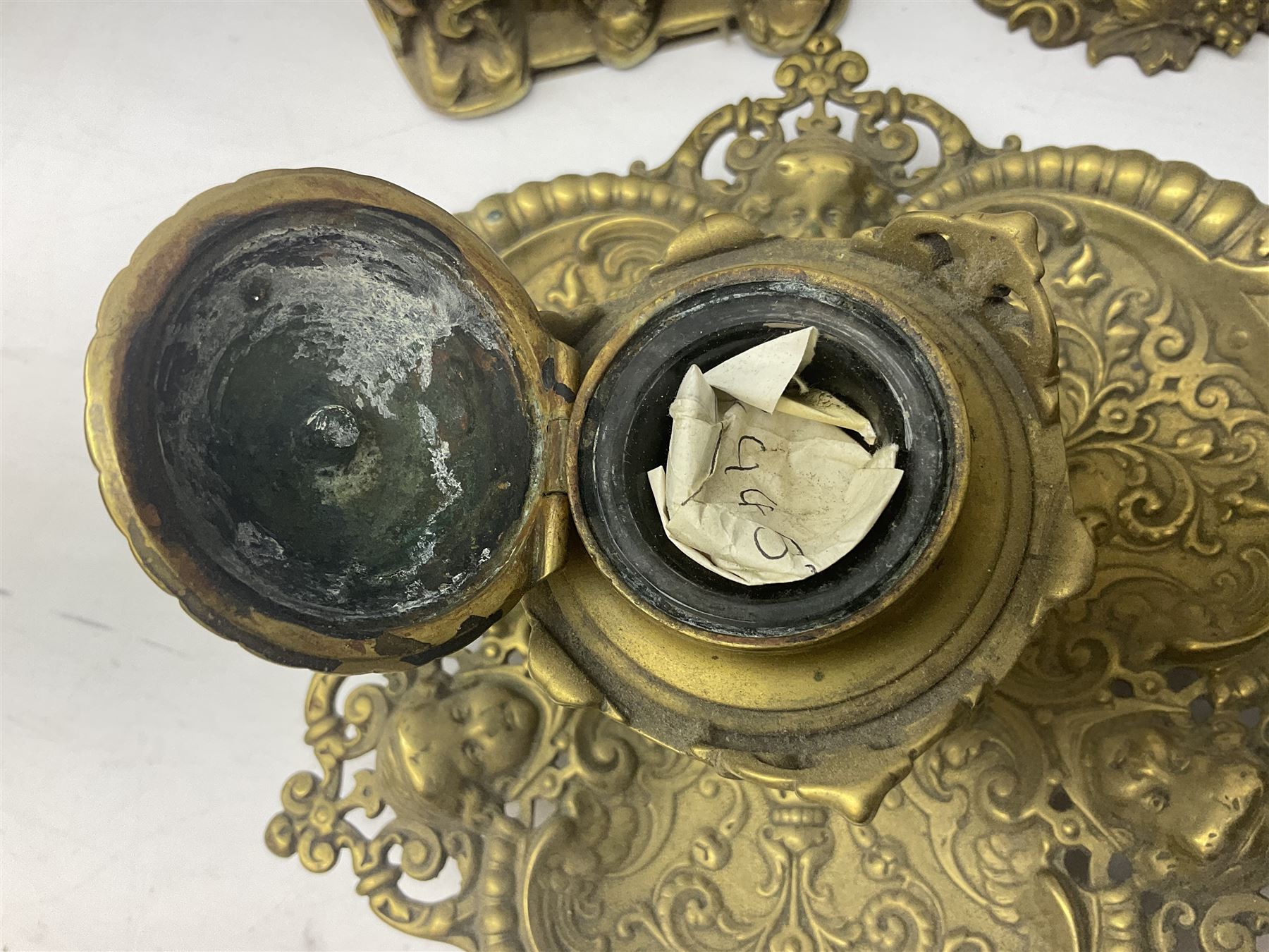 Collection of victorian and later brass desk accessories, to include a letter holder with cherub design, ink well of square form with hinged lid, brass table bell, brass casket with relief decoration, etc  