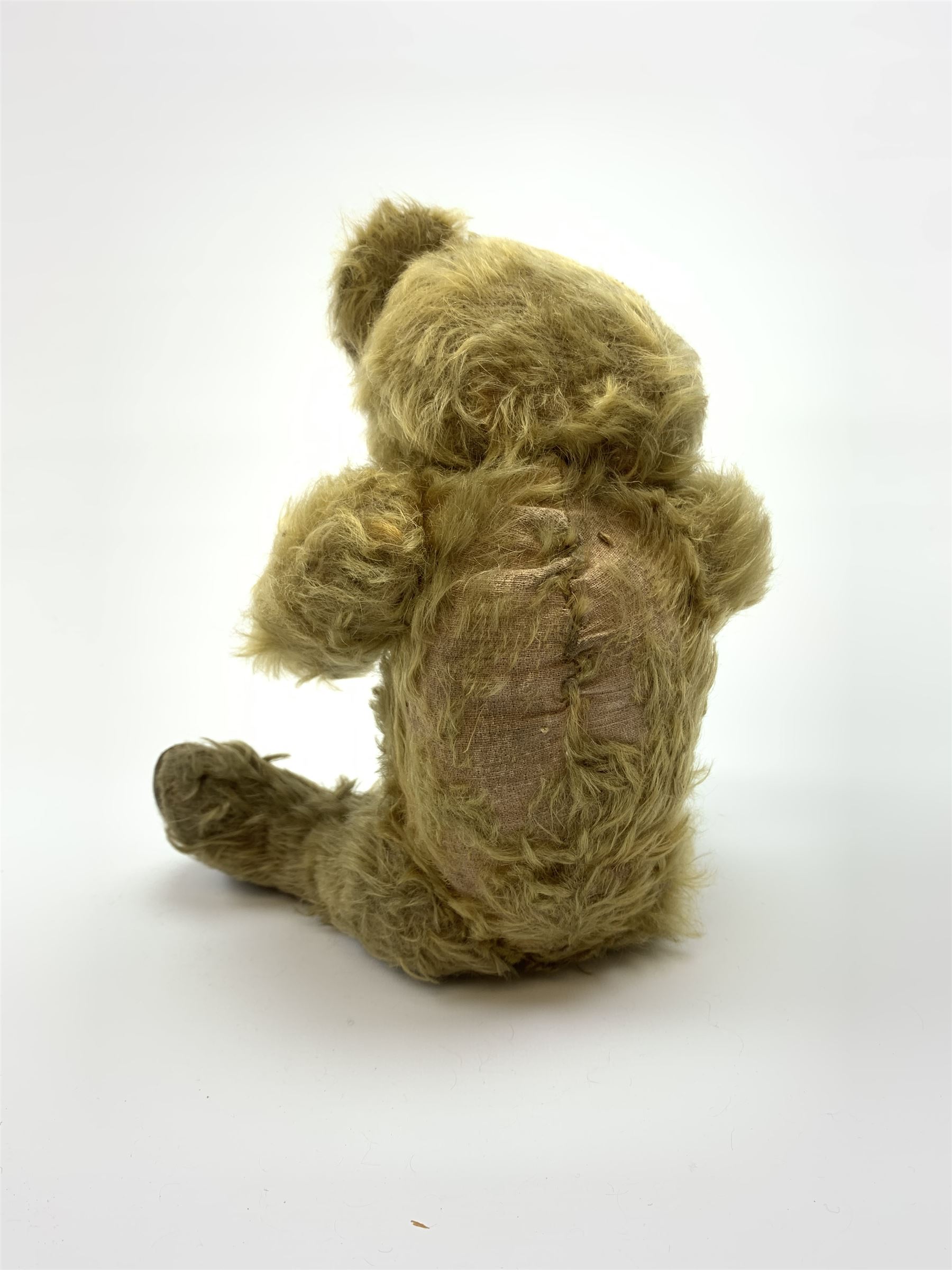 Early 20th century English teddy bear, WW1 period, with wood wool filled mohair body, fixed head with one boot button eye and vertically stitched nose and mouth and jointed limbs with cloth paw pads H16