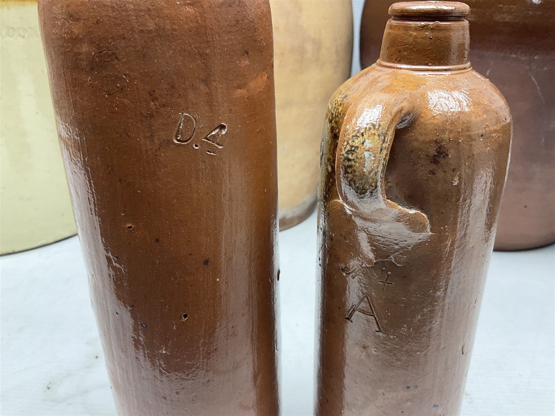 Quantity of stoneware flagons, to include Skipton, Clitheroe and Hellifield related examples, four salt glazed bottles, large cylindrical stoneware jar, large twin handled jar and vase, together with two brass jam pans, tallest H35cm