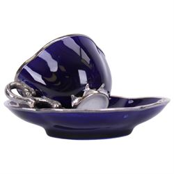 Cranberry glass scent bottle with silver overlay, together with German fluted vase with silver overlay upon a blue ground and similar teacup