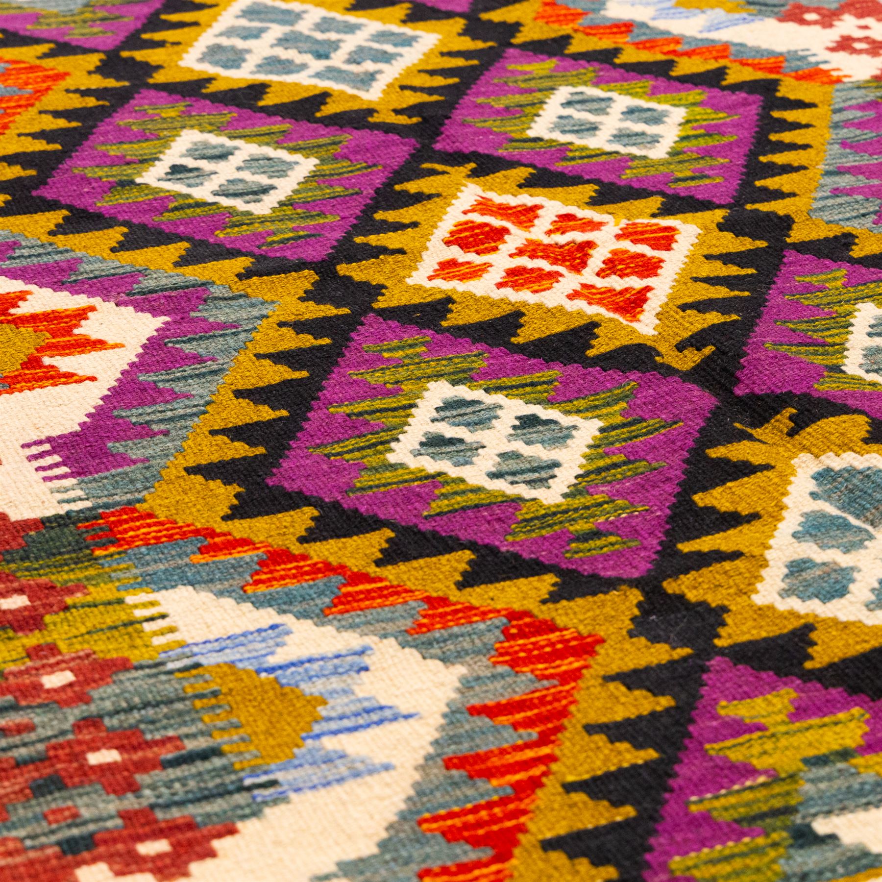 Afghan Maimana flatweave kilim, central field features large bold nested diamond motifs and stylized geometric lozenge patterns on olive purple, blue, and green tone ground, border stripe in teal ground, and fringe