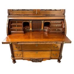 Large and impressive late 19th century Irish mahogany secretaire bookcase, moulded sloped arch dentil pediment decorated with central carved mask surrounded by linen festoons and trailing bellflowers, canted and fluted uprights with carved acanthus leaf upper and lower brackets, enclosed by two astragal glazed doors in the form of trophies with twist ribbon carved mouldings, inlaid with fanned spandrels and trailing leaf painted satinwood band, cylinder roll top inlaid with central fan motif and fanned spandrels, pull-out action revealing stepped fitted interior, central tambour roll cupboard flanked by two Composite pilasters and a combination of drawers and pigeon holes, fitted with three break-front drawers, matched canted and fluted corners with acanthus leaf carvings, on square tapering and fluted spade feet