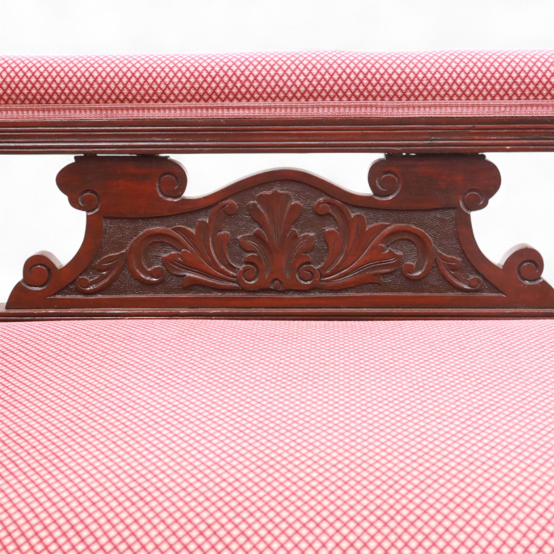 Late Victorian mahogany chaise longue, of scroll-ended form, upholstered in red diamond-patterned fabric with padded back and scroll-carved support, open arm with carved foliate and turned upright, raised on turned tapering legs 
