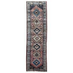 Persian Yalameh coral ground runner rug, the field decorated with seven hooked lozenge medallions surrounded by stylised plant motifs, the indigo spandrels decorated with similar patterns, guarded border with repeating diamond lozenges