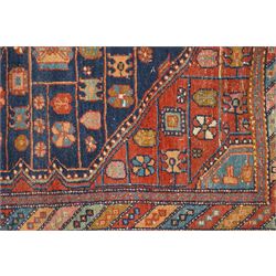 Persian Heriz hand-knotted carpet, terracotta ground centred by large dark navy geometric medallion with stepped outline, decorated throughout with stylised flowerheads, palmettes and geometric motifs in blue, green and ochre, enclosed by diagonal geometric border with narrow guard stripes