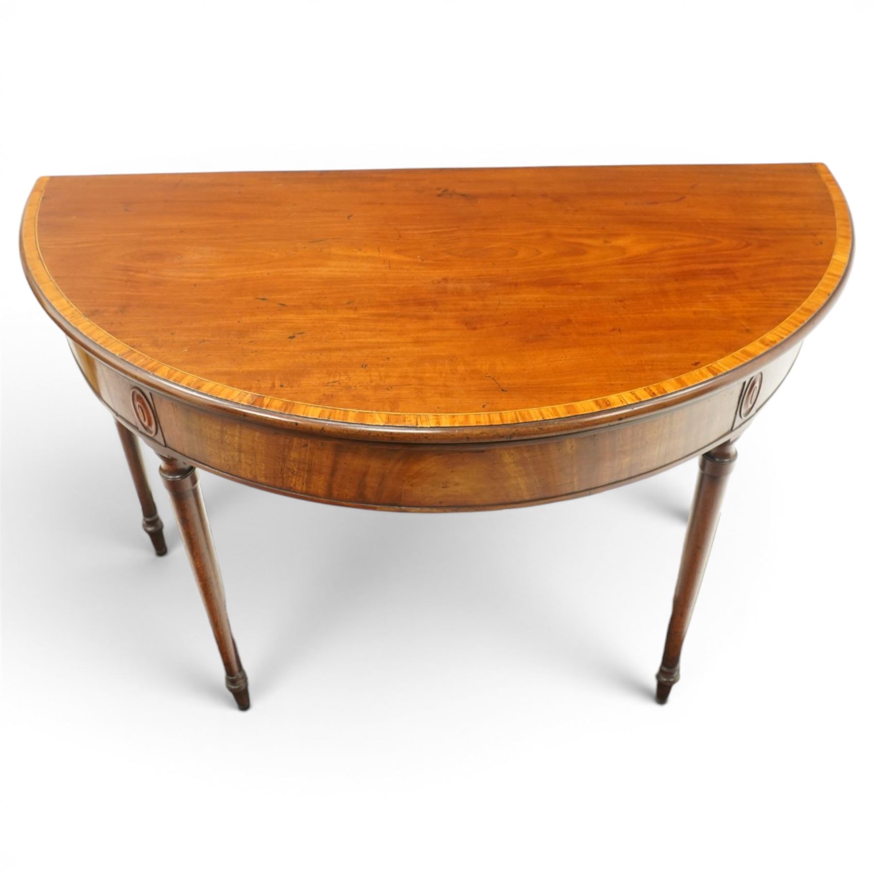 Georgian mahogany demi-lune card table, the lunette shaped top with cross-banded and boxwood-strung edge, opening to reveal baize-lined interior and supported by rear gatelegs, over a banded frieze with applied oval plaques, raised on turned and tapering supports