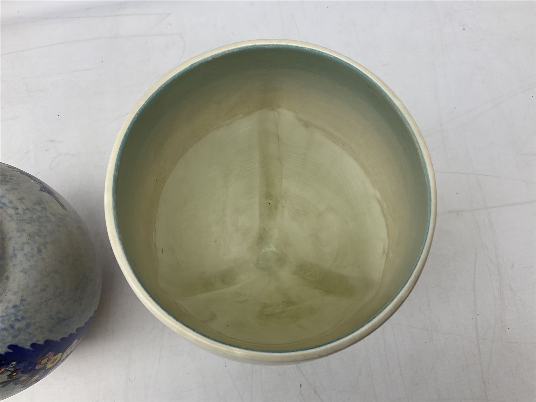 1930s Carlton Ware Art Deco Garden pattern vase of shouldered ovoid form, decorated with blue, pink and yellow flower heads on a mottled blue and white ground, pattern no. 3413, with printed and painted marks beneath, H19cm, together with a Clarice Cliff My Garden pattern vase, raised upon three feet with blue, pink and purple moulded Hollyhock design, H20cm, with Clarice Cliff Wilkinson Ltd England marks beneath