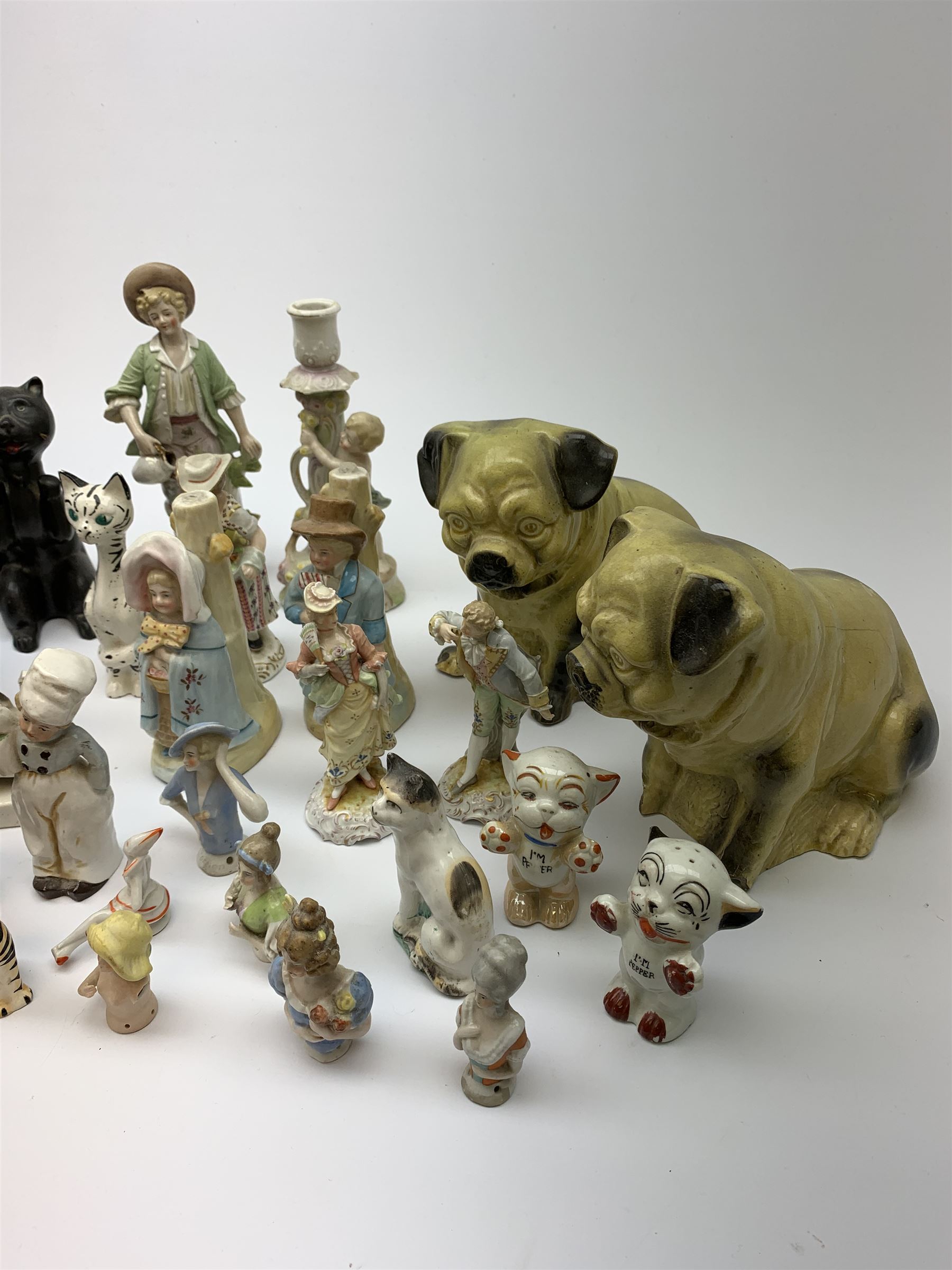 A collection of various ceramic figurines, to include pair of small 19th century Staffordshire cats, Royal Doulton cat, Coalport cat, pair of 19th century pug dogs, two fairings inscribed Good Templars, two Bonzo dog peppers, a number of pin cushion dolls, various 20th century and later black pottery cats, Victorian bisque figures, etc. 